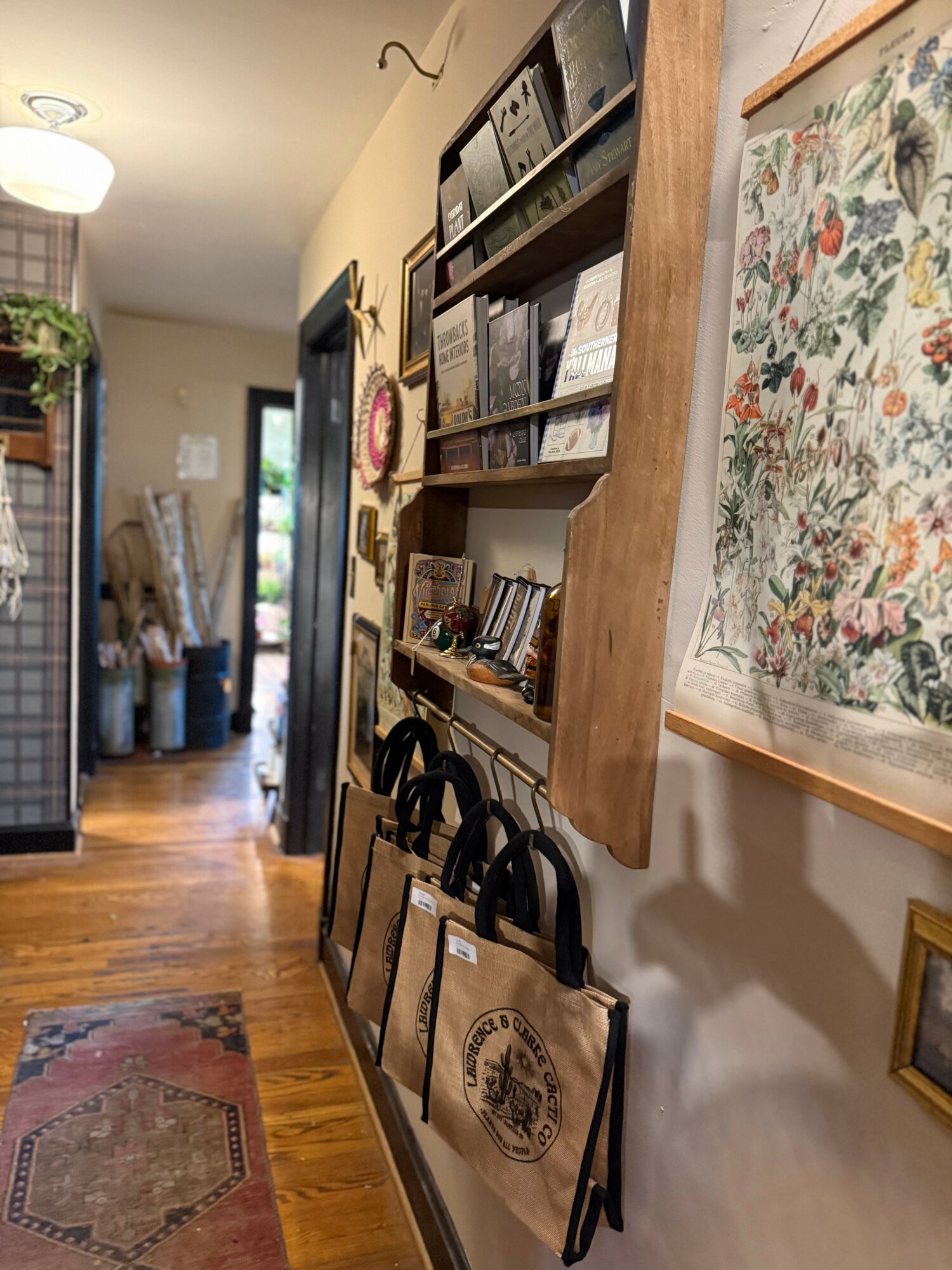 Hallway with shelves, framed artwork, and a door leading outside, wooden flooring, and a rug.