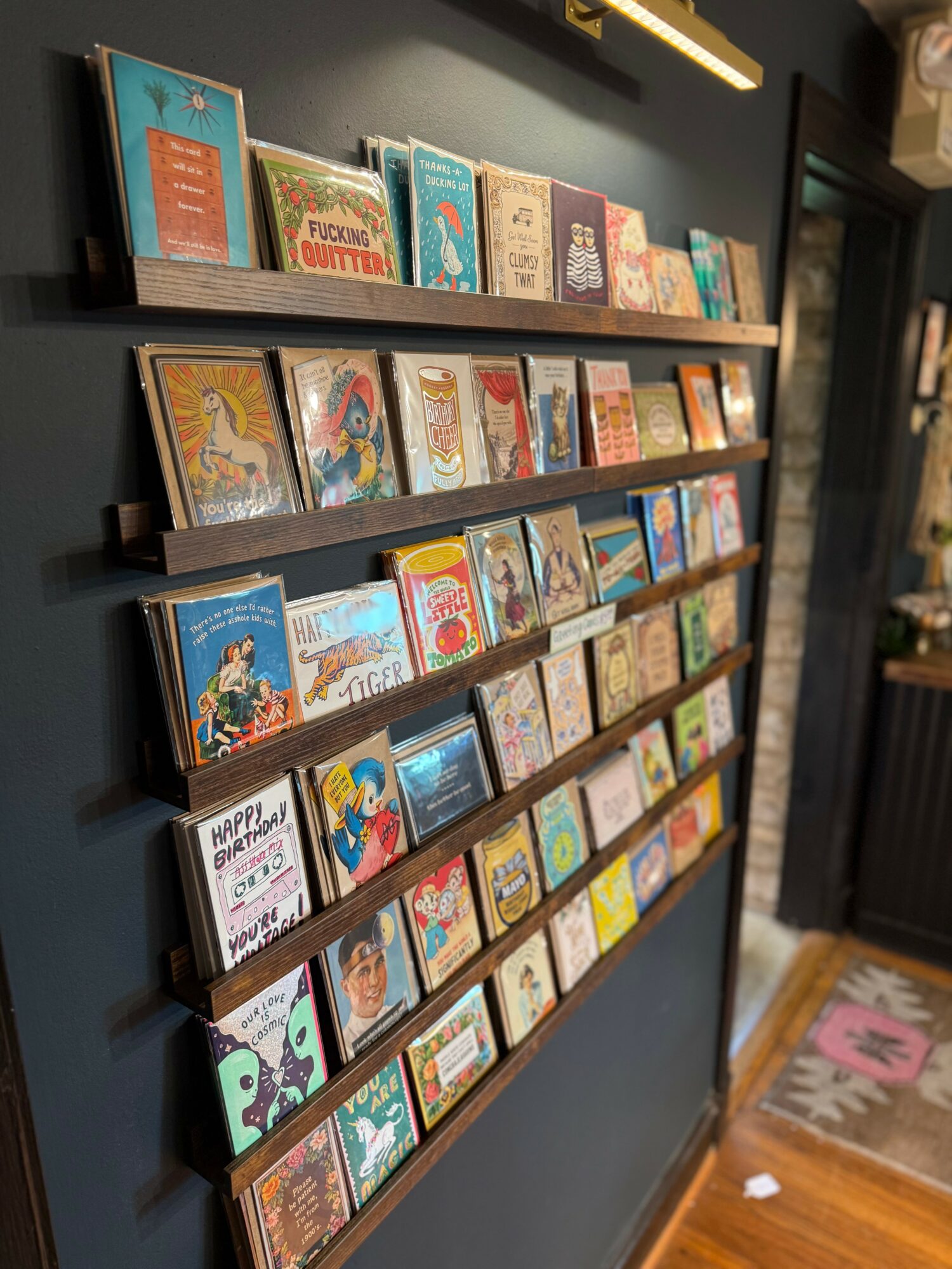 Books displayed on a wall-mounted wooden shelf with multiple rows, colorful covers, in a cozy indoor setting.