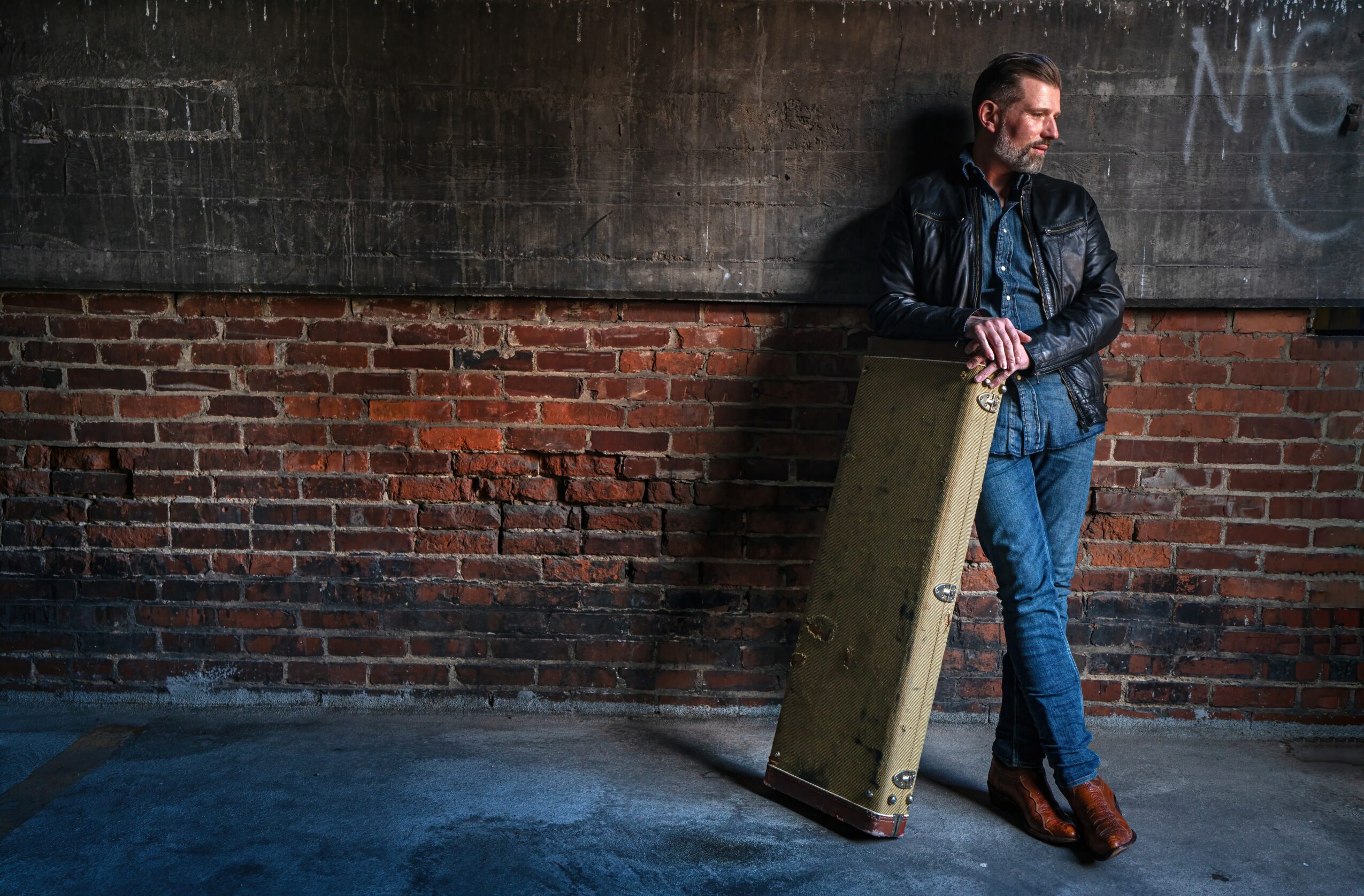 Man leaning against a brick wall holding a large rectangular object, outdoors at night.