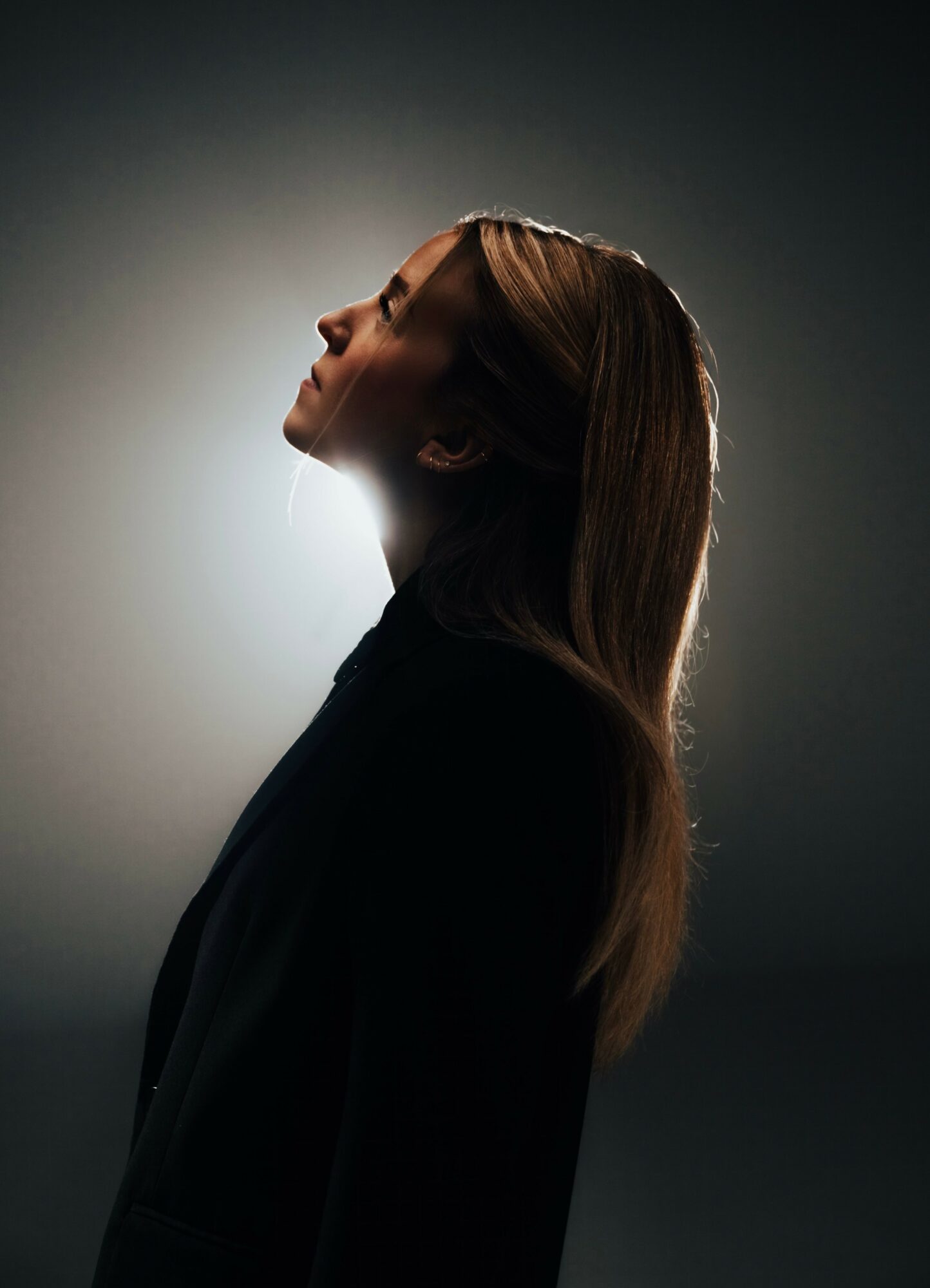 Silhouette of a woman with long hair, head tilted back, backlit with a halo effect, dark background.