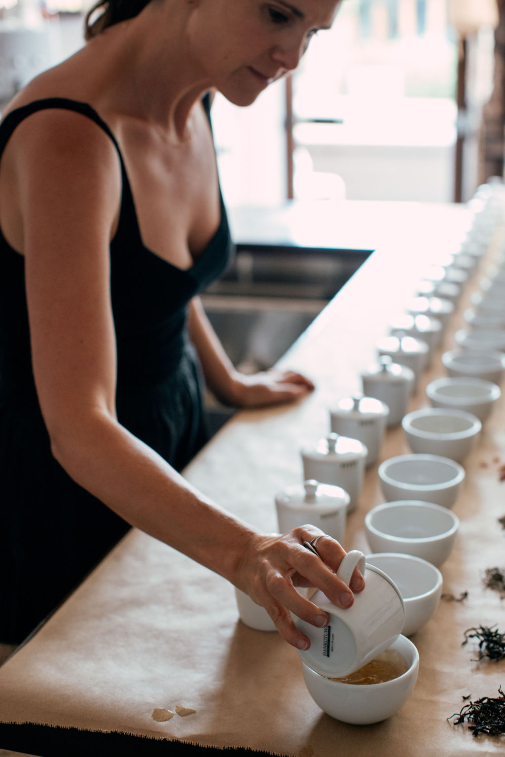 Woman in black dress arranging white cups on a table in a bright room.