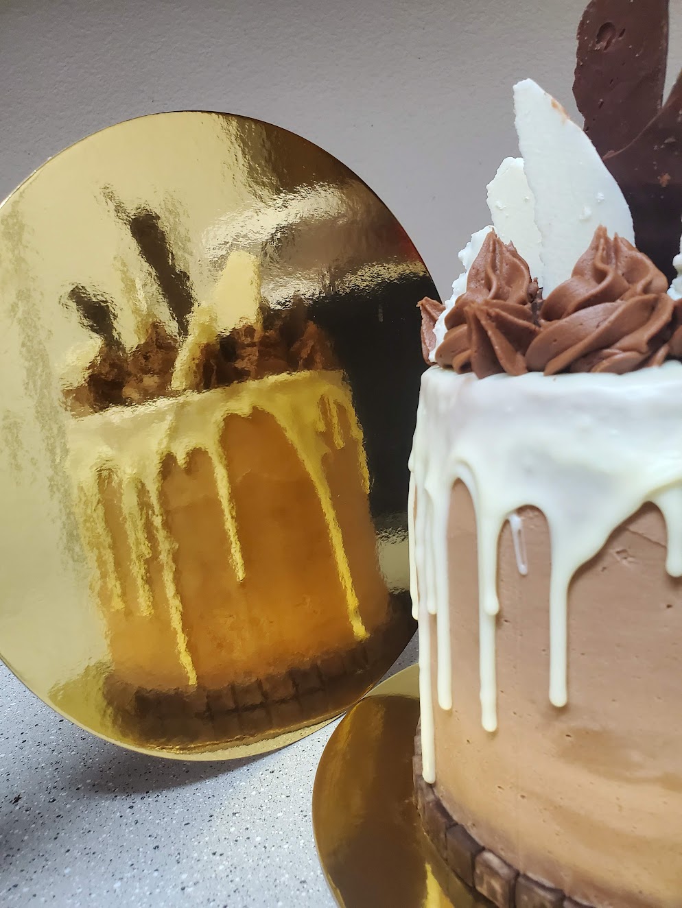 Cake with white and chocolate frosting, topped with chocolate swirls and a white decorative element, reflected in a shiny gold sphere.