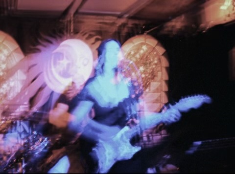 Person playing guitar on stage with colorful lights and blurred motion effects.