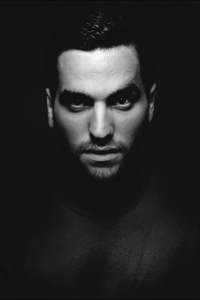Black and white portrait of a man with intense expression, looking directly at the camera, with shadows emphasizing facial features.