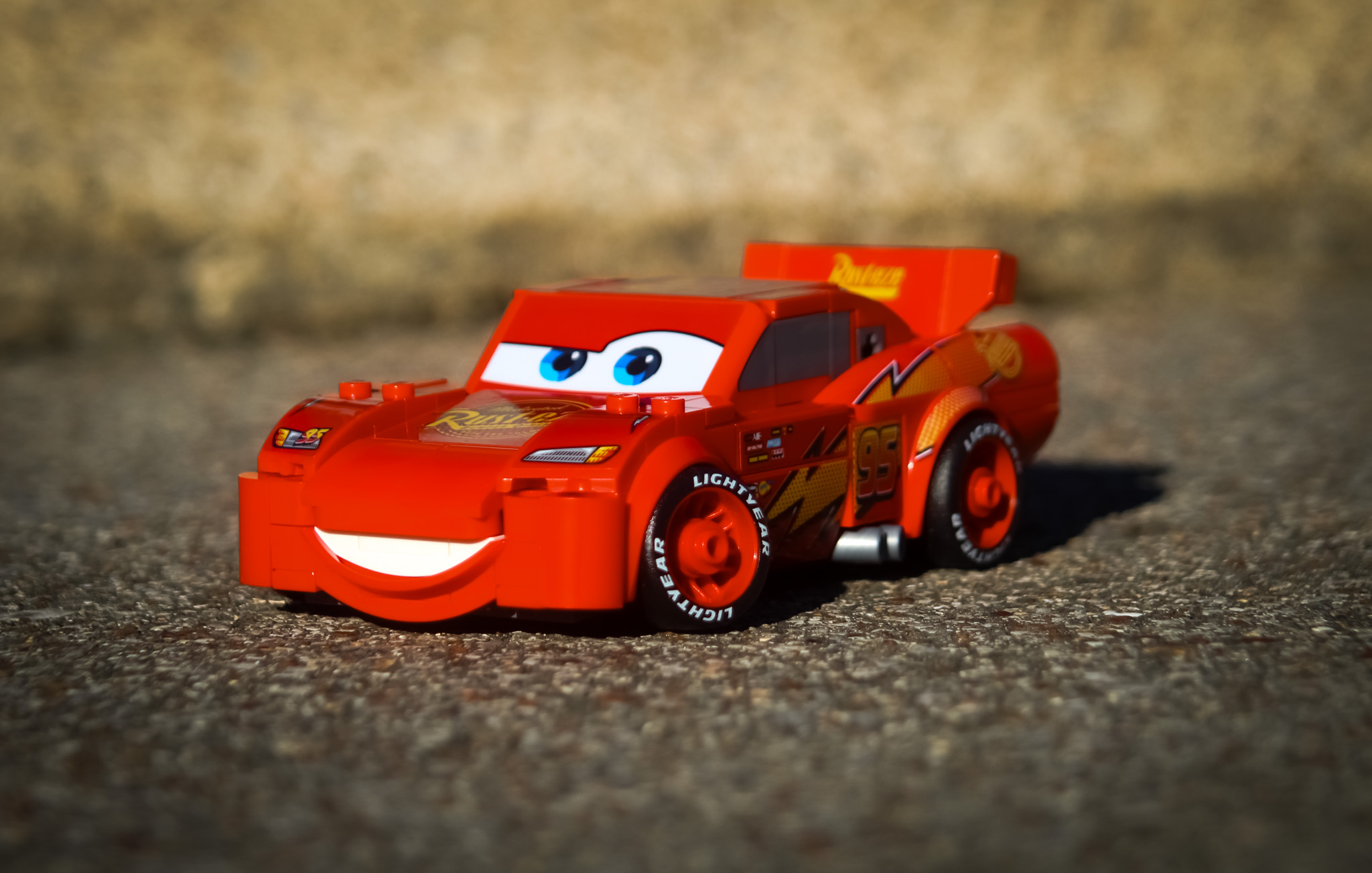 Red toy race car with smiling face and blue eyes on a textured surface, background blurred.