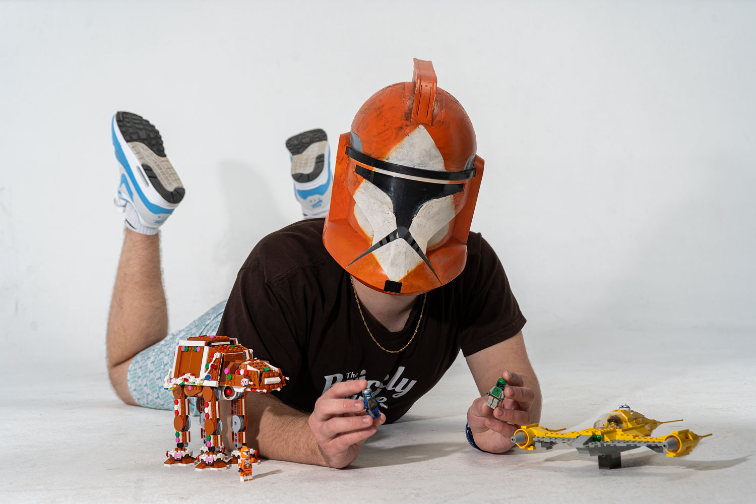 Child wearing a Star Wars helmet, lying on stomach, playing with toys on a white background.