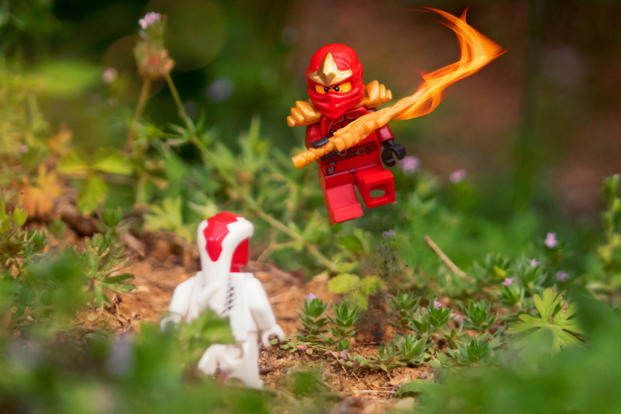Lego ninja figure flying with a flaming sword above a small white dinosaur toy in a garden setting.