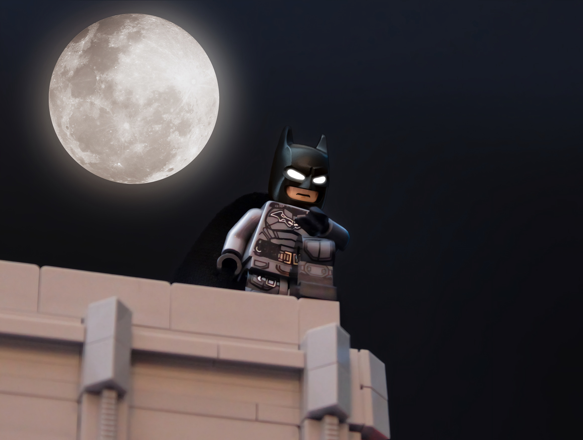 LEGO Batman figure stands on a rooftop against a full moon in a dark sky.