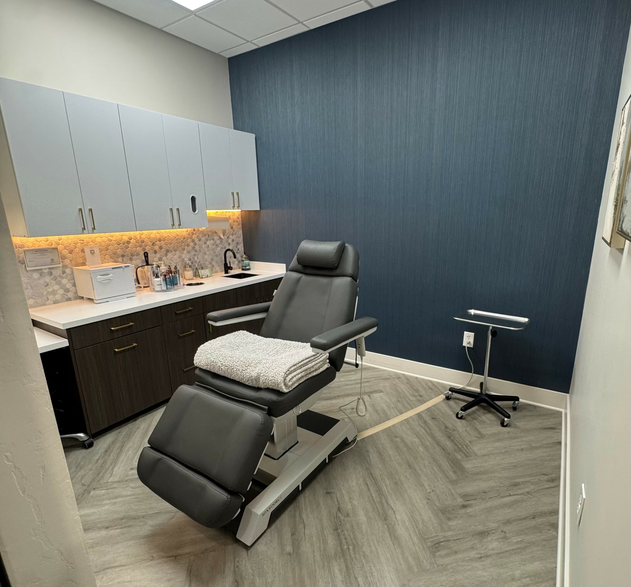Medical examination room with a reclining chair, cabinets, and a small table, in a modern setting.