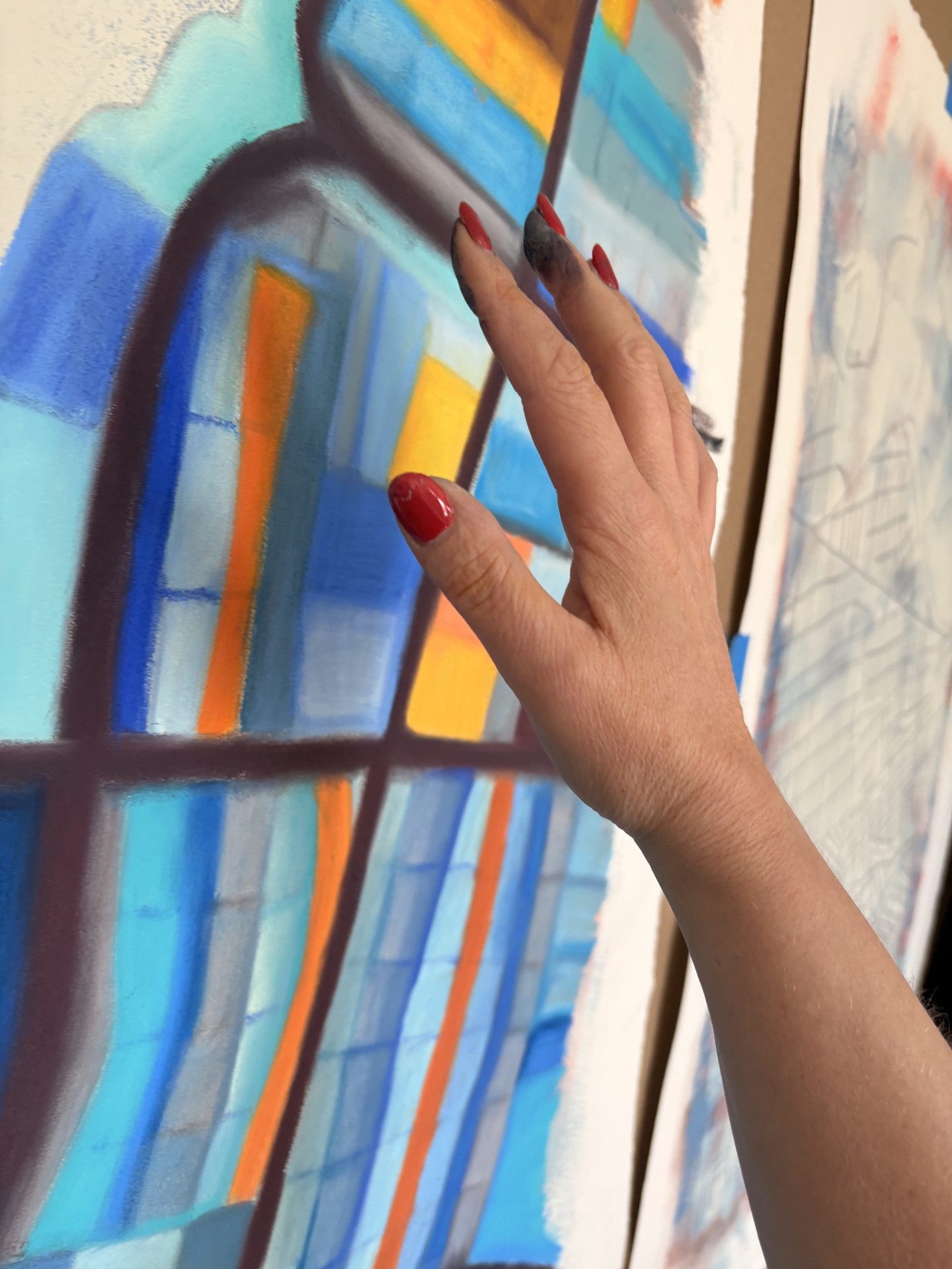 Person's hand with red nail polish touching a colorful abstract painting on a wall.