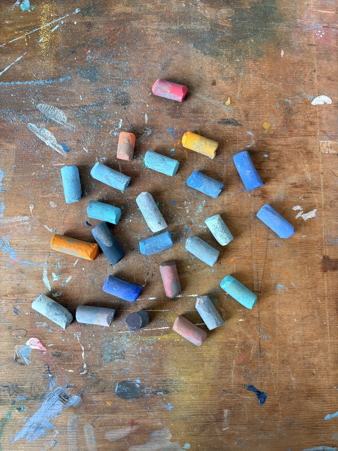 Colorful chalk pieces scattered on a wooden surface with paint marks and scratches.