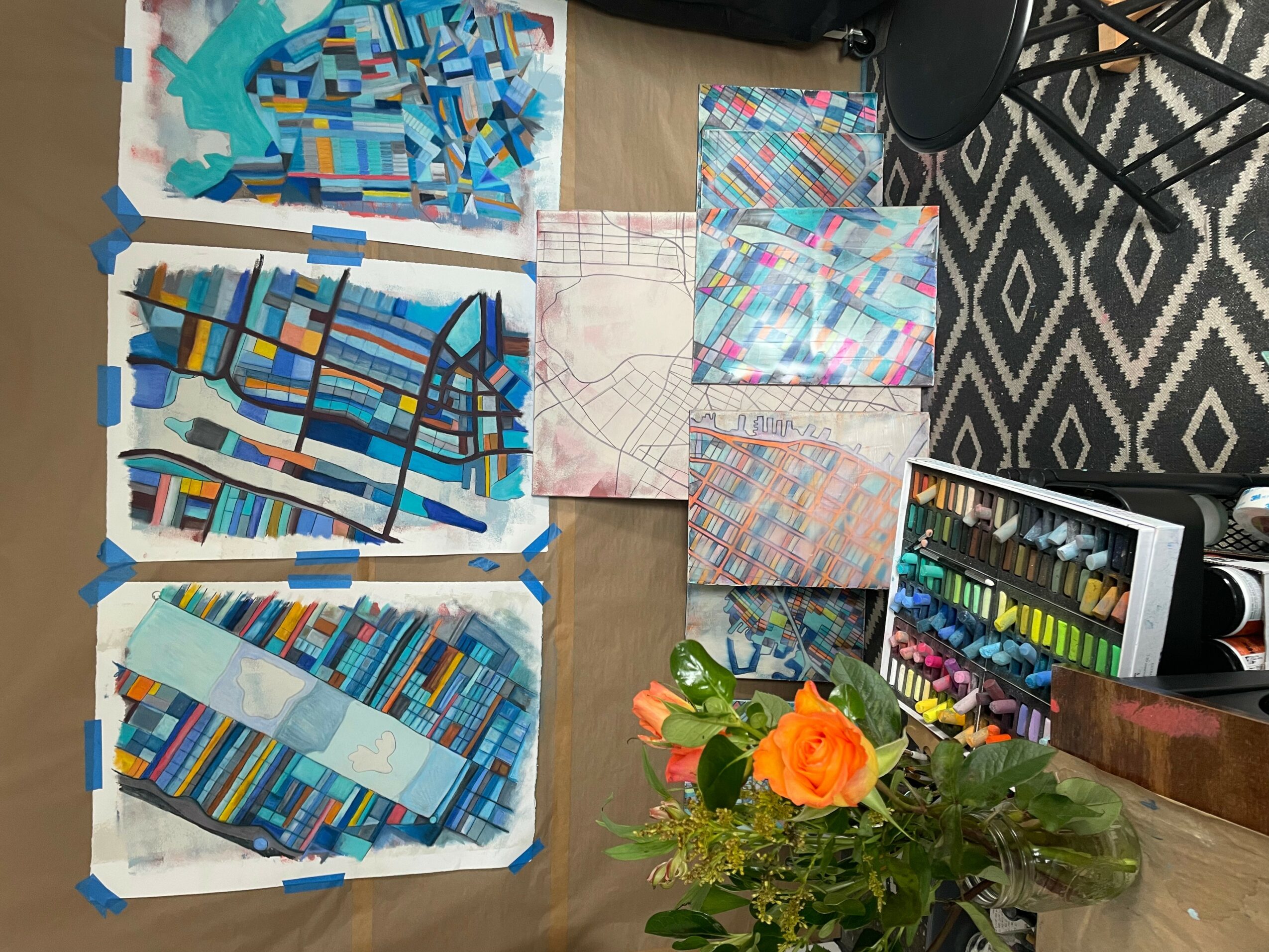 Six fabric pieces with colorful geometric patterns are taped to a table, with a flower arrangement and a box of markers nearby.