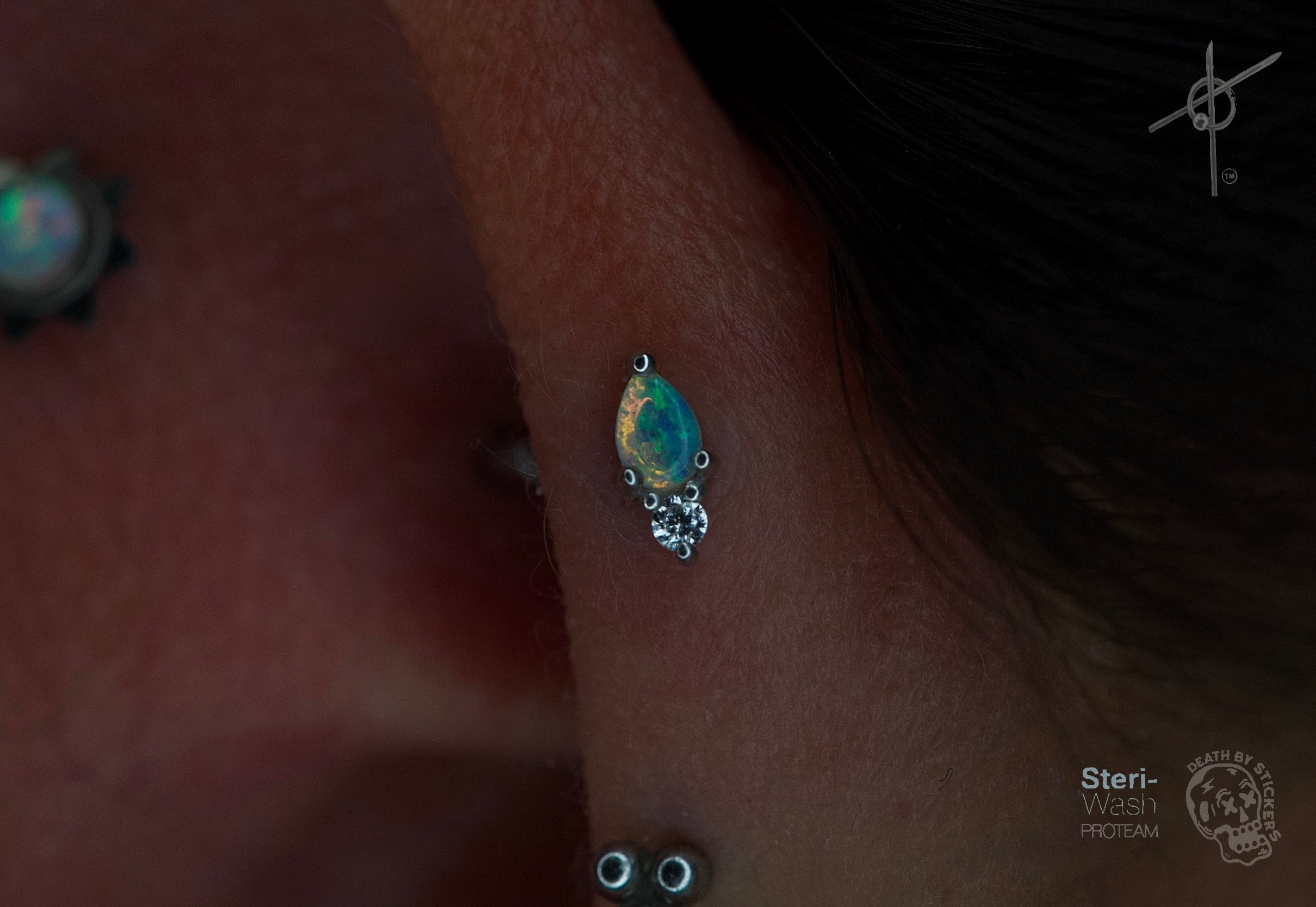 Close-up of a person's ear with a turquoise and silver earring, and a small black piercing below the earlobe.