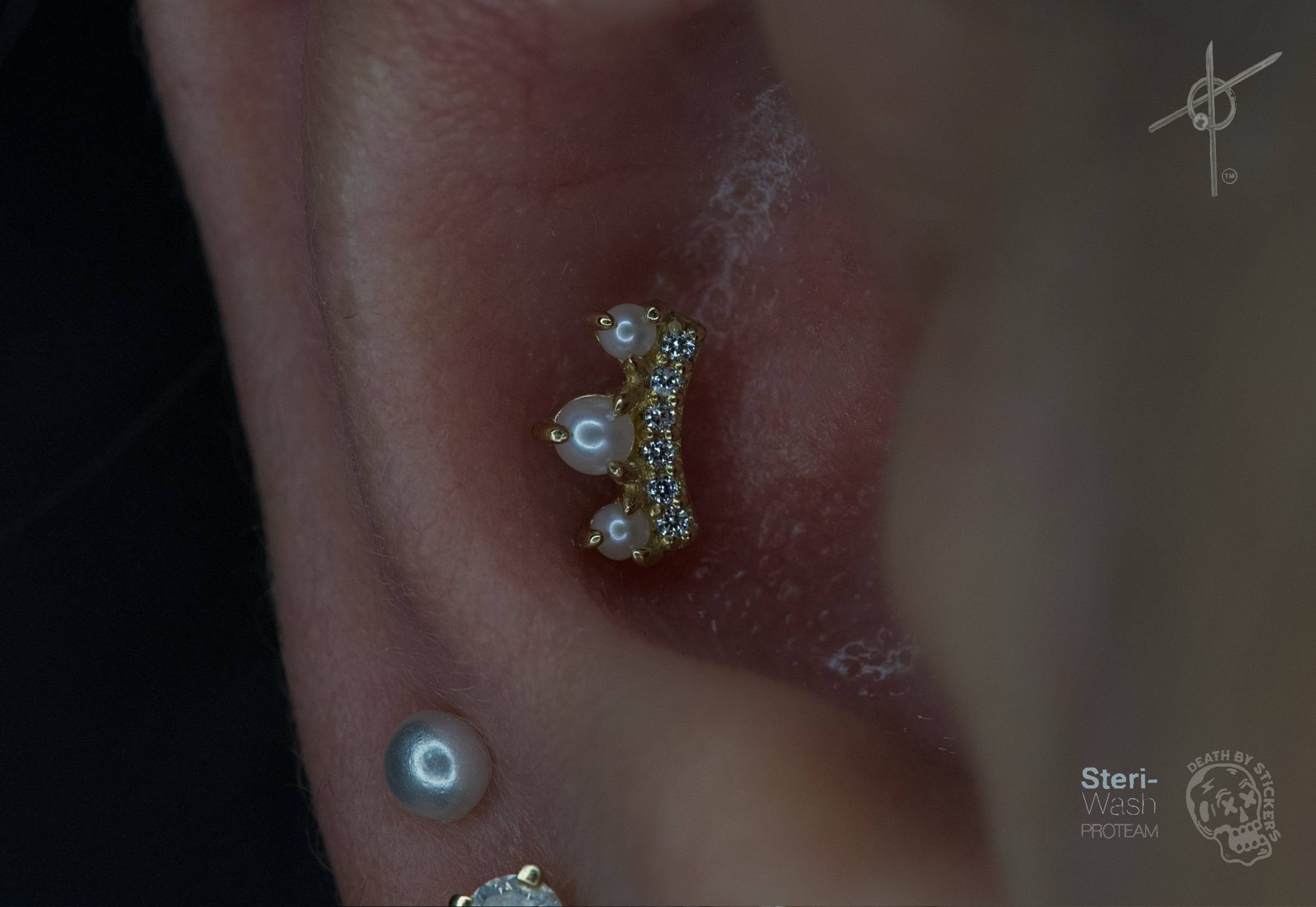 Close-up of a pierced ear with a gold and pearl earring, and a small pearl stud below, against a dark background.