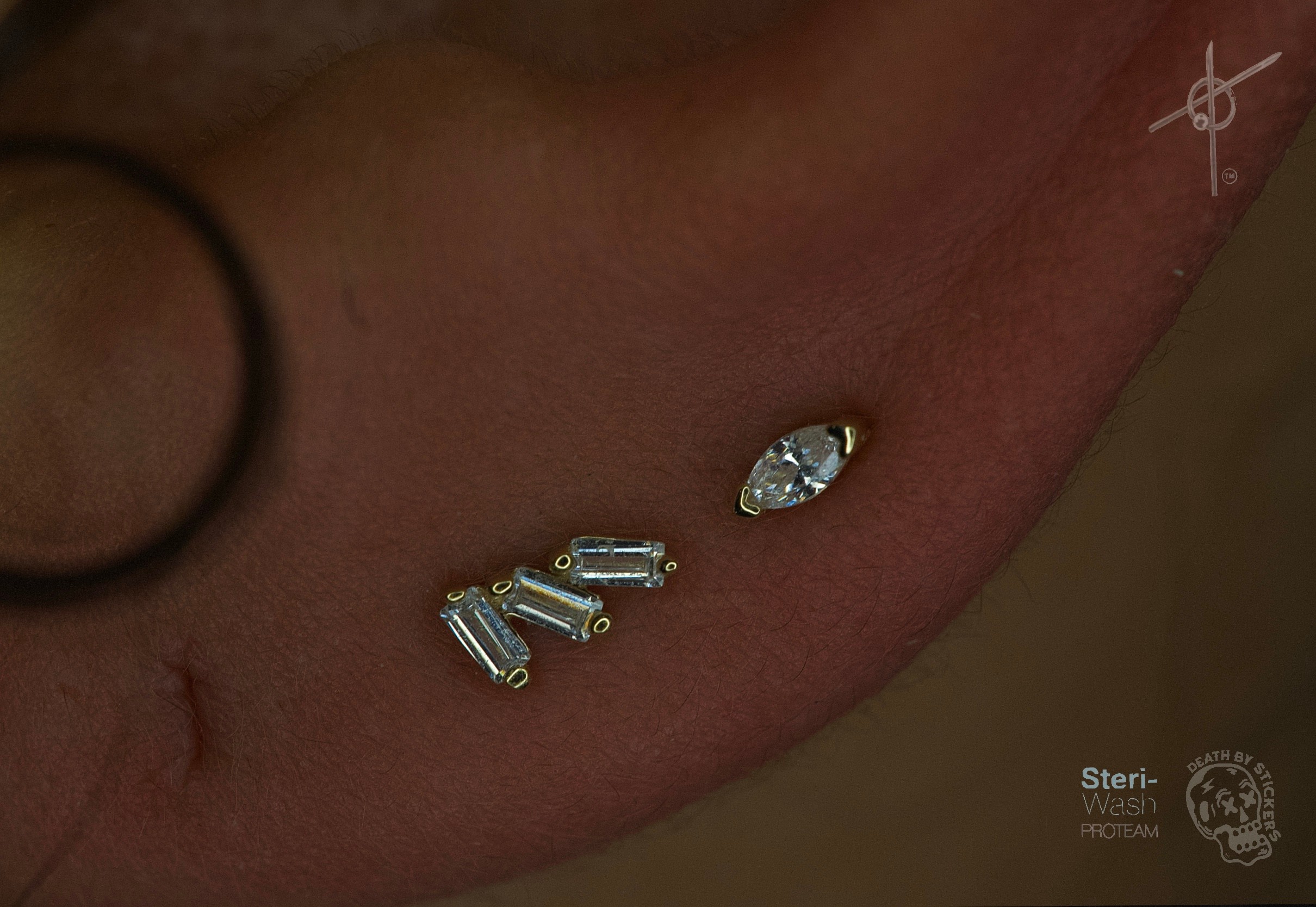 Close-up of a person's skin with multiple small jewelry pieces and a larger gemstone piercing.