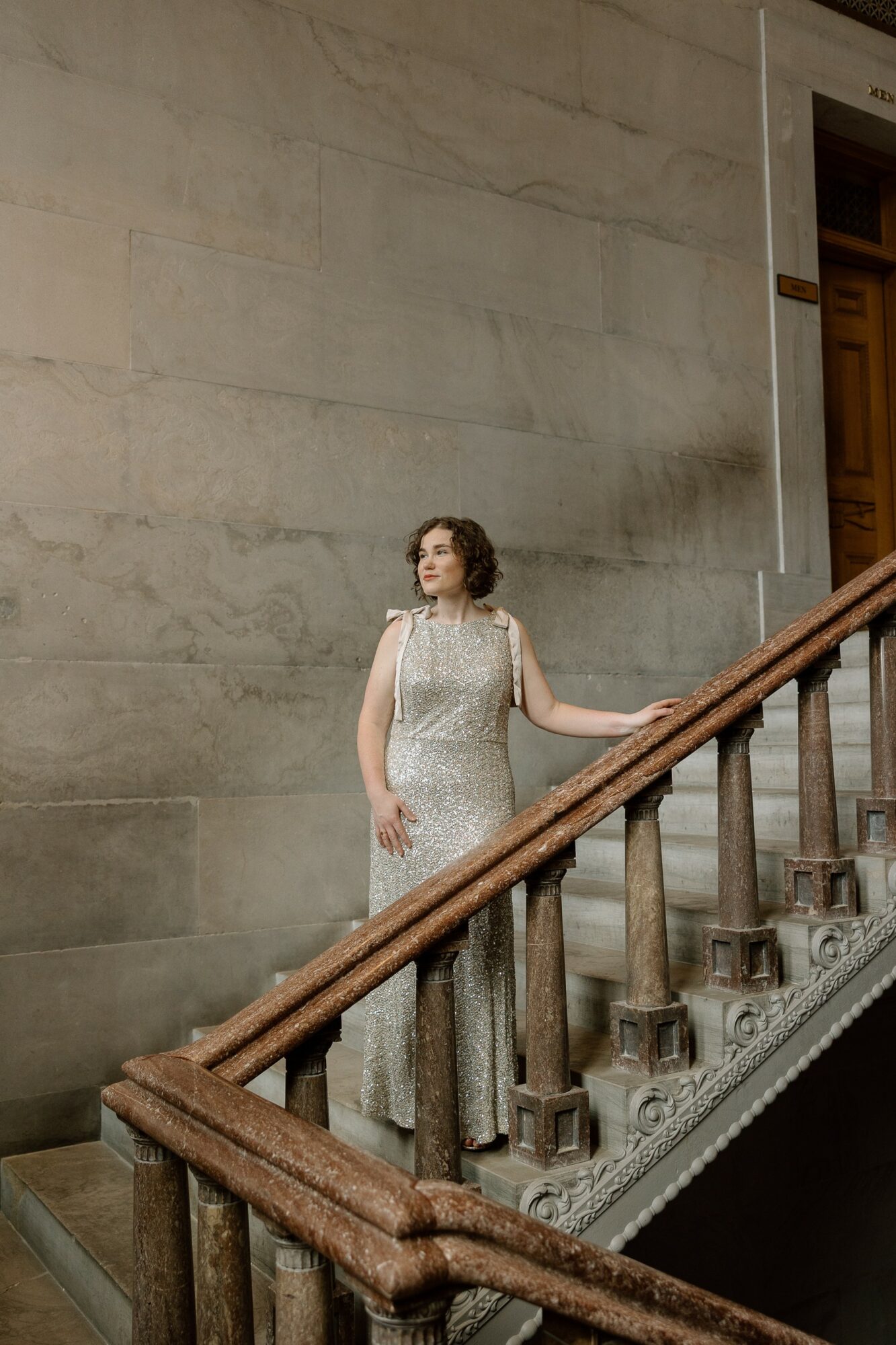 Woman in a long, elegant dress standing on a staircase with a large stone wall background.