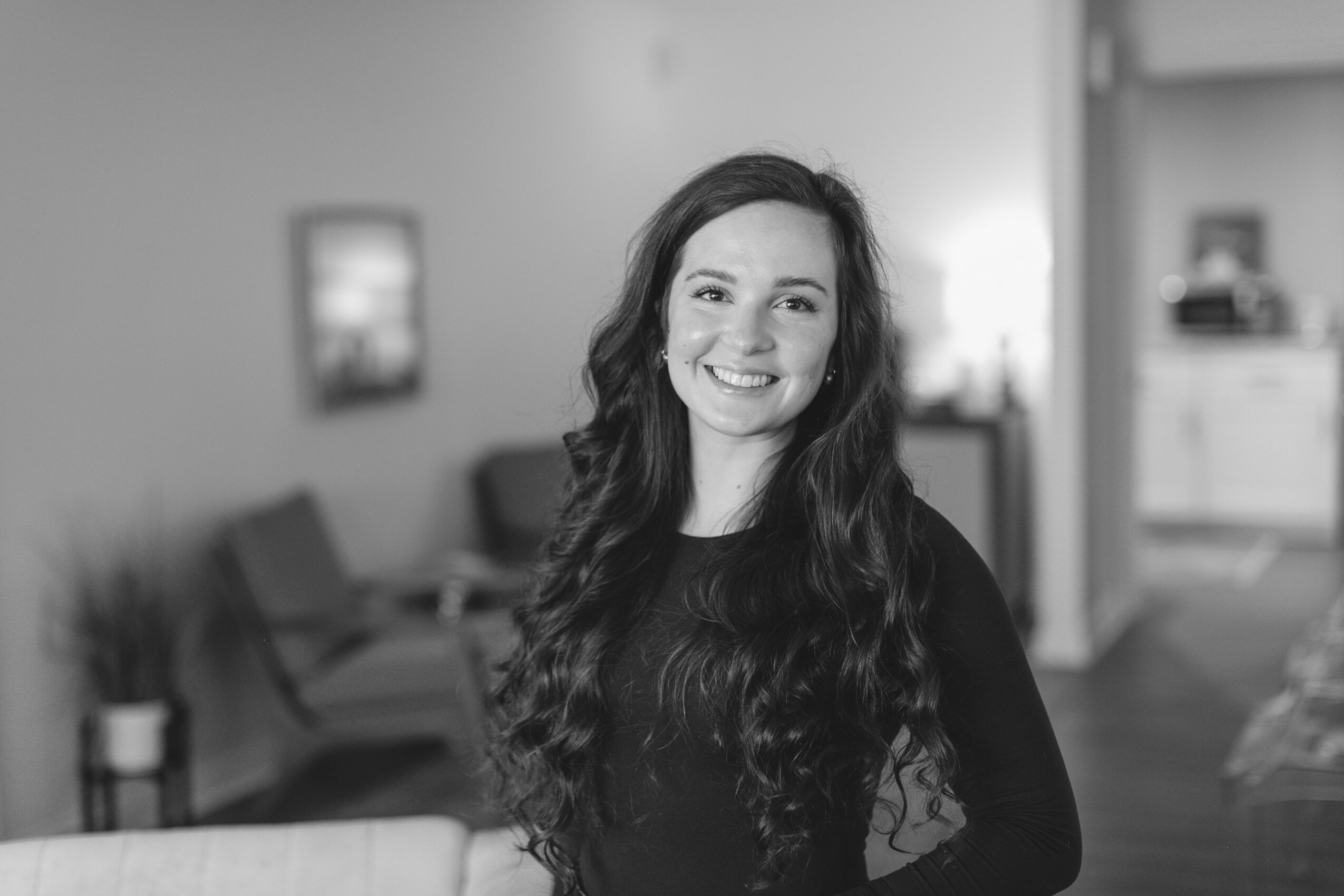 Smiling woman with long wavy hair in a living room, black and white photo.