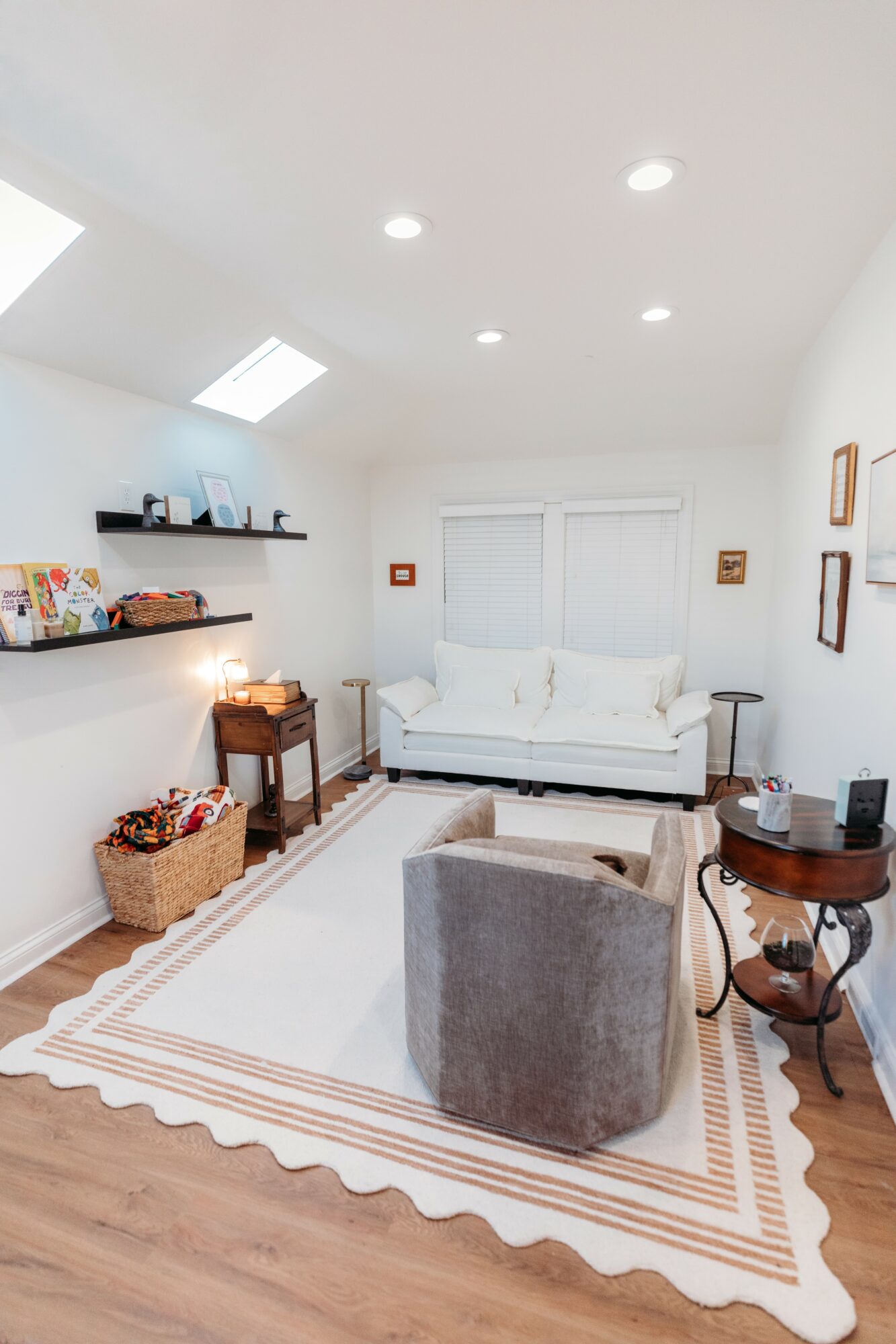 Living room with white walls, ceiling lights, a white sofa, gray armchair, wooden side table, and a striped rug.