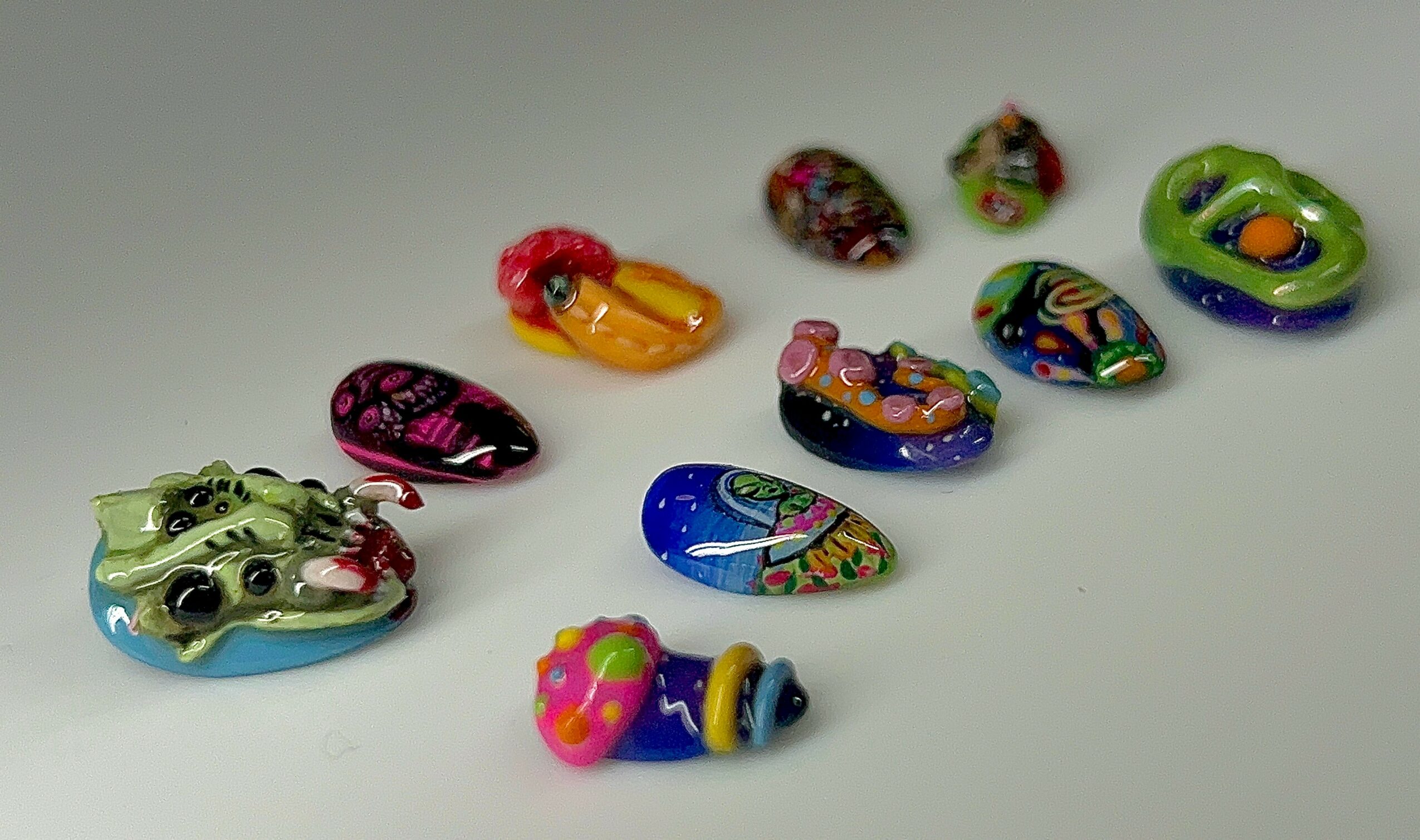 Colorful painted rocks with various designs on a white surface, some resembling animals or objects.