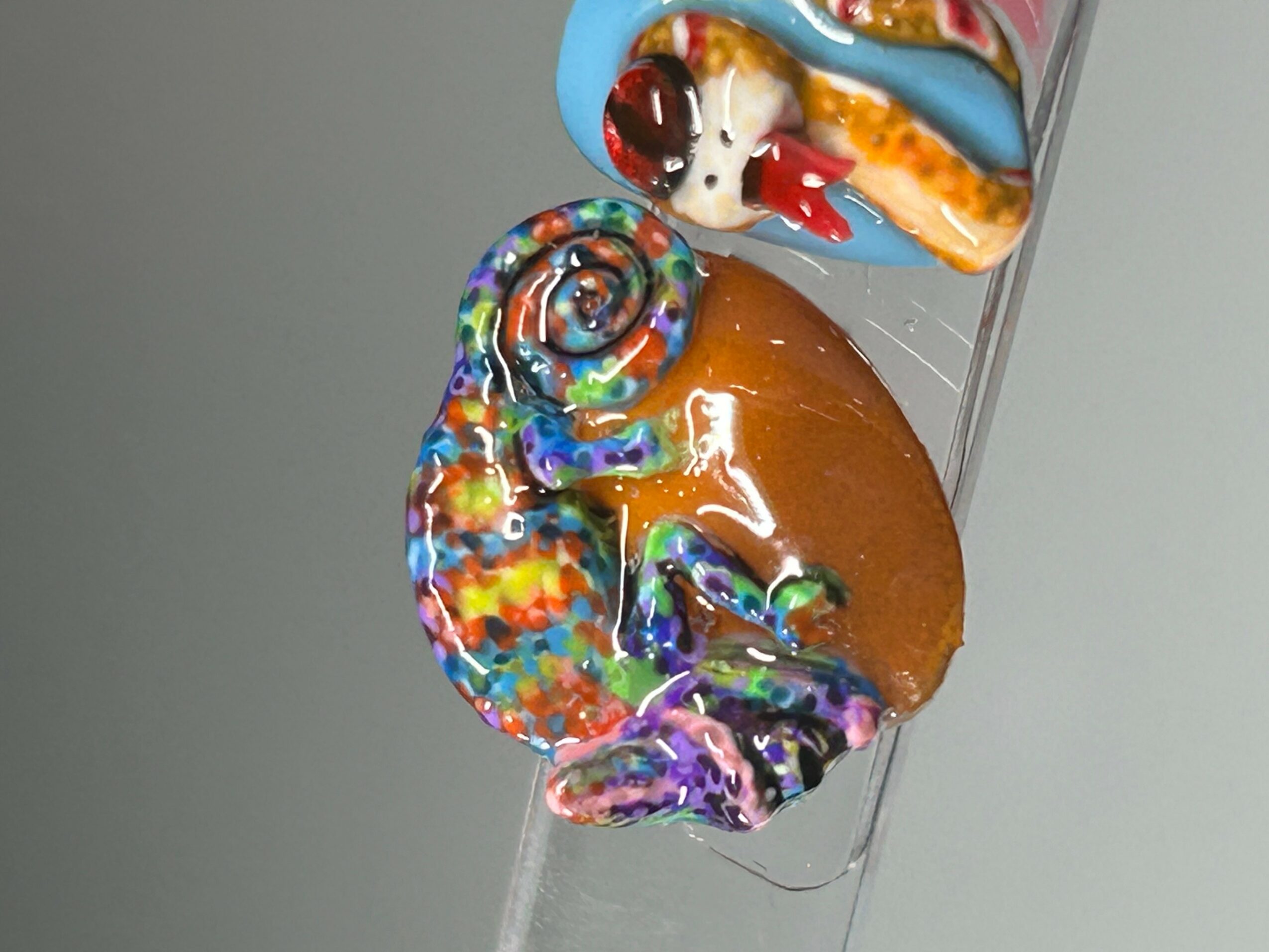 Colorful decorated donut with rainbow sprinkles and a small decorated cookie on a clear surface.
