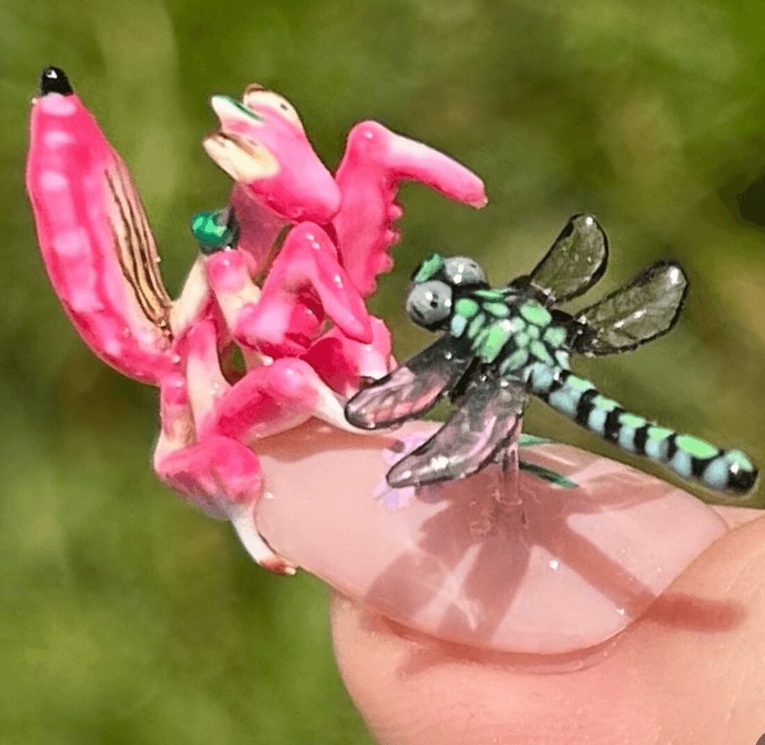 Pink plastic flamingo and a green and black dragonfly toy on a finger, with a blurred green background.