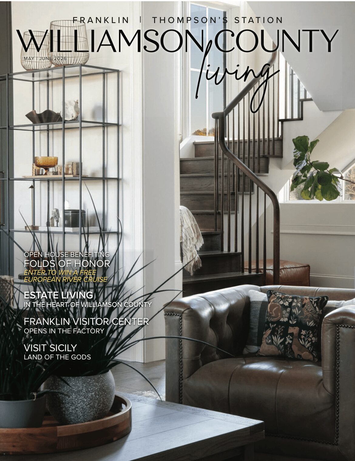 Interior view of a living room with a staircase, a leather sofa, and a glass display cabinet, bright natural light.