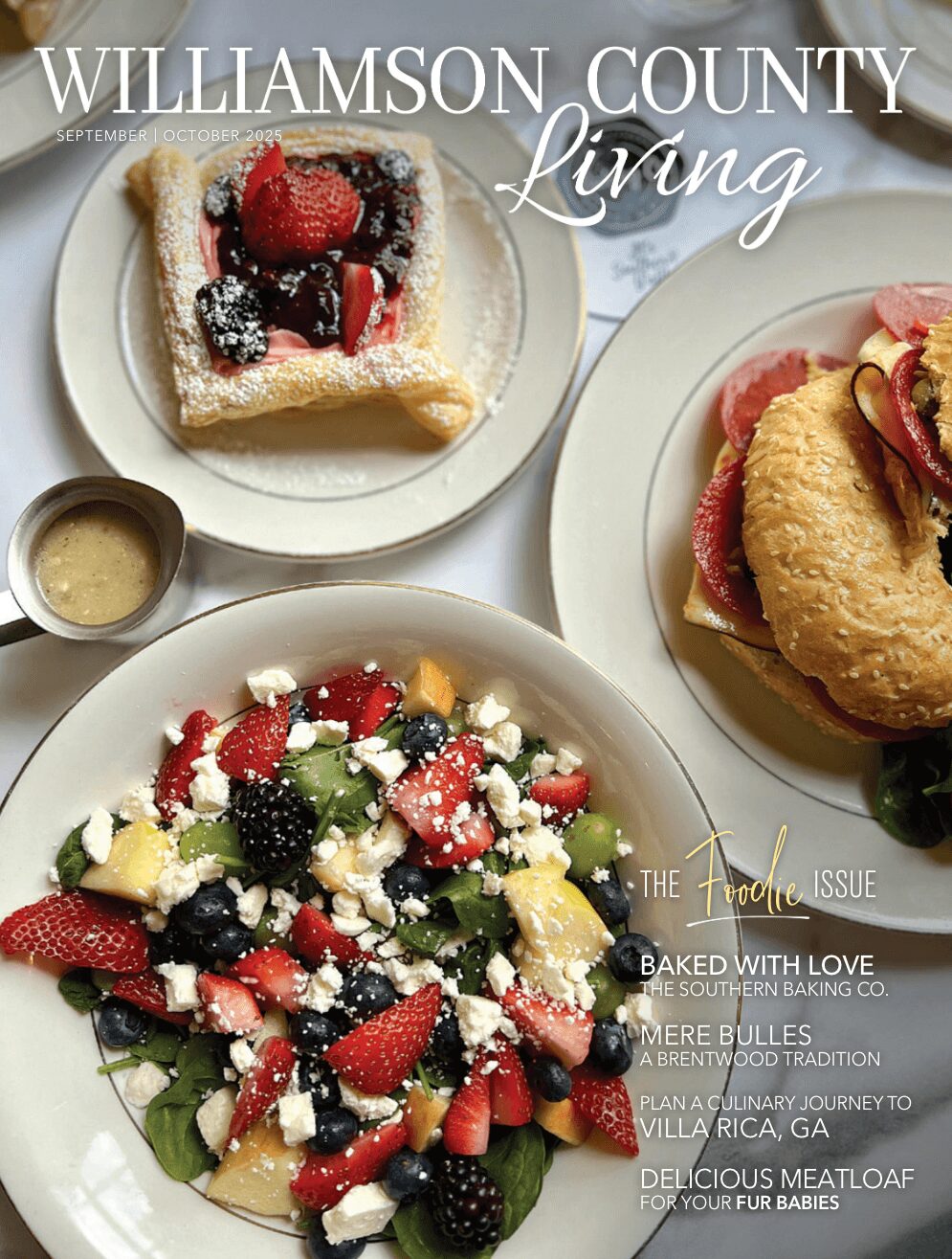 Three plates of food: a fruit tart, a sandwich with fried chicken, and a salad with berries and cheese, on a white table.