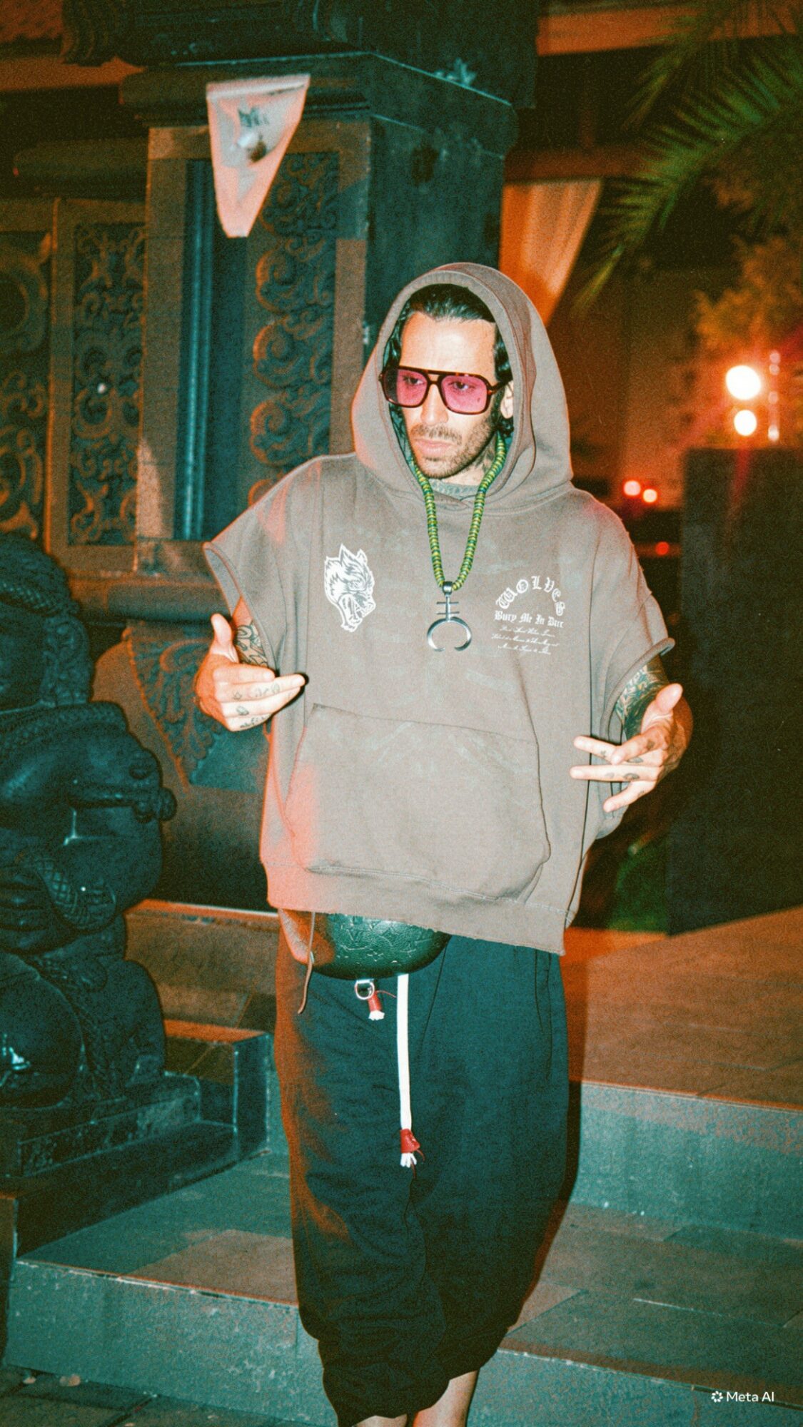 Person wearing glasses and a hoodie, standing outdoors at night, making peace signs with both hands.
