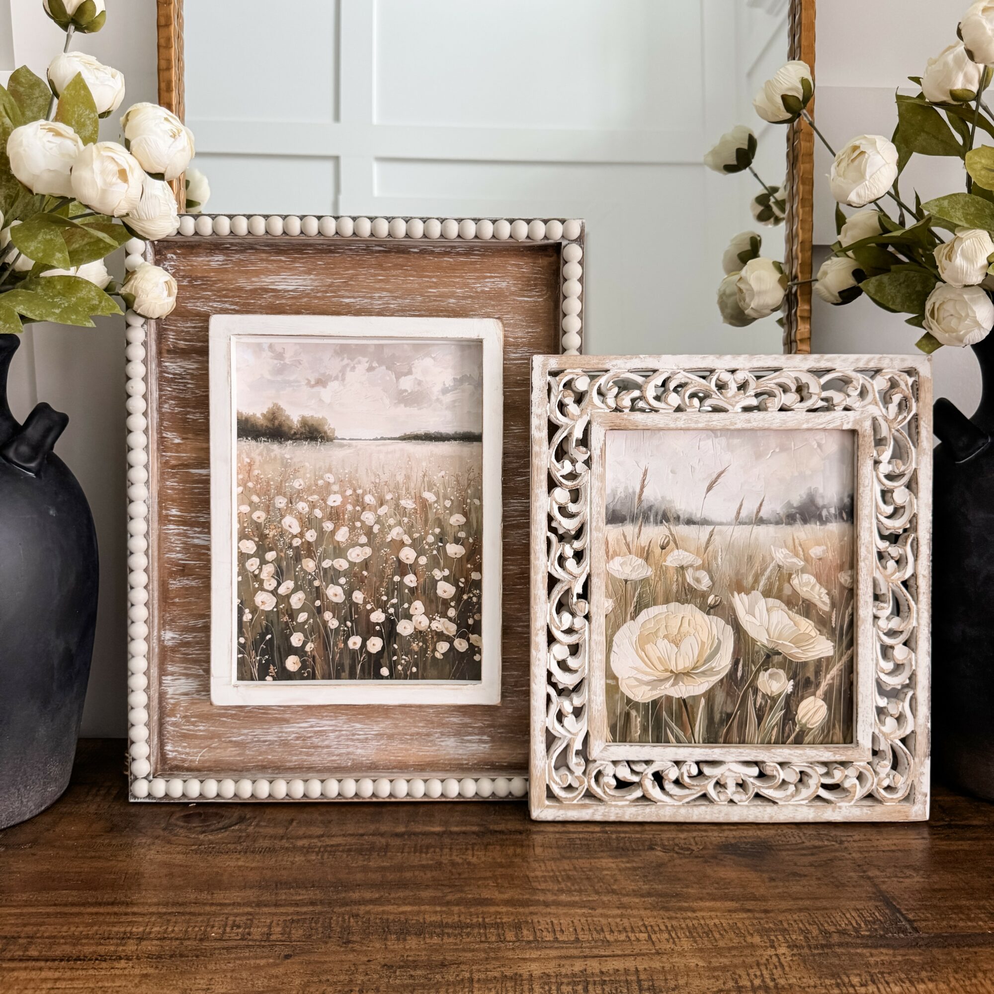 Two framed floral paintings on a wooden surface, with white flowers in vases on either side.