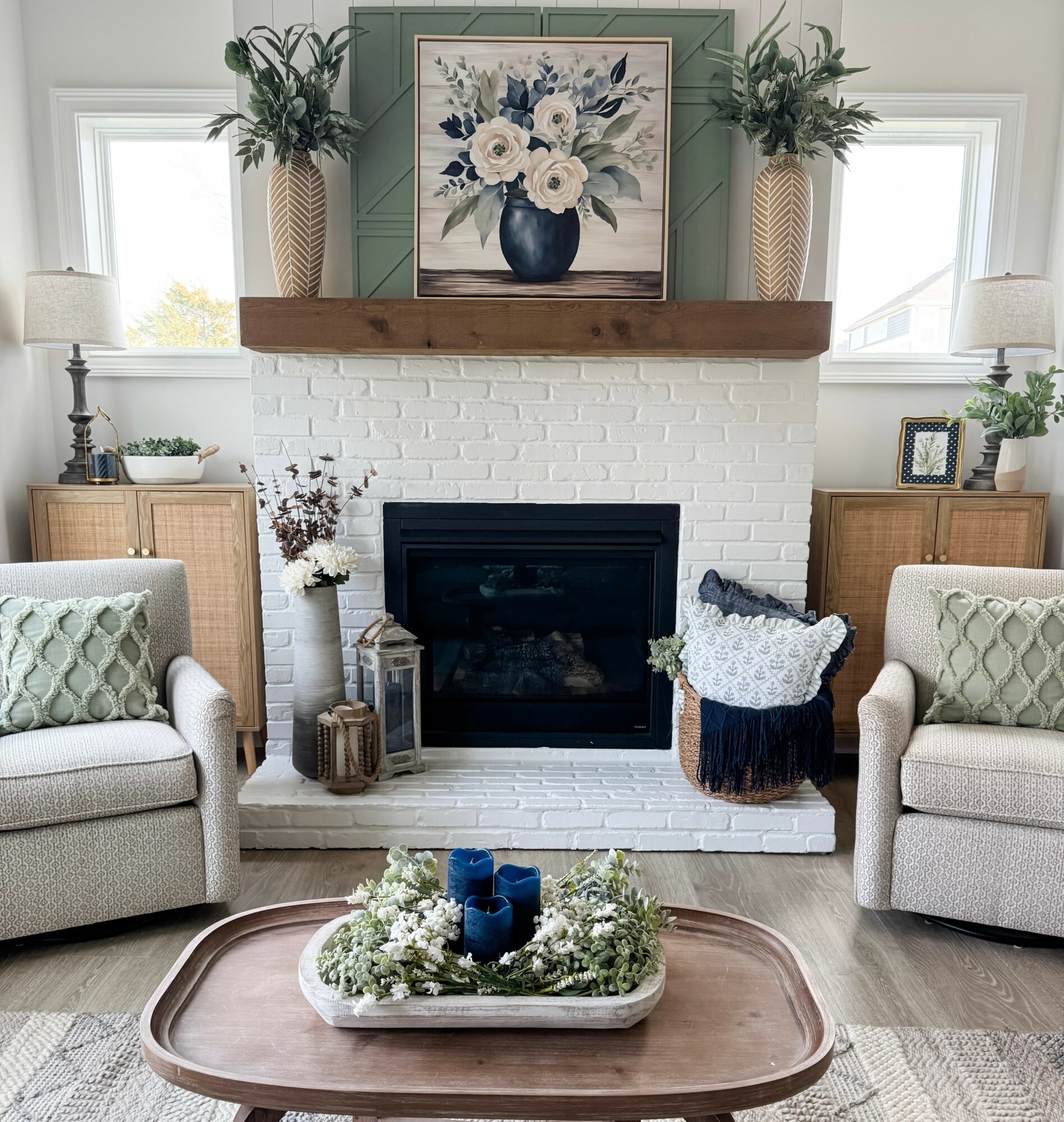 Living room with white brick fireplace, two armchairs, and a wooden coffee table with candles and greenery.