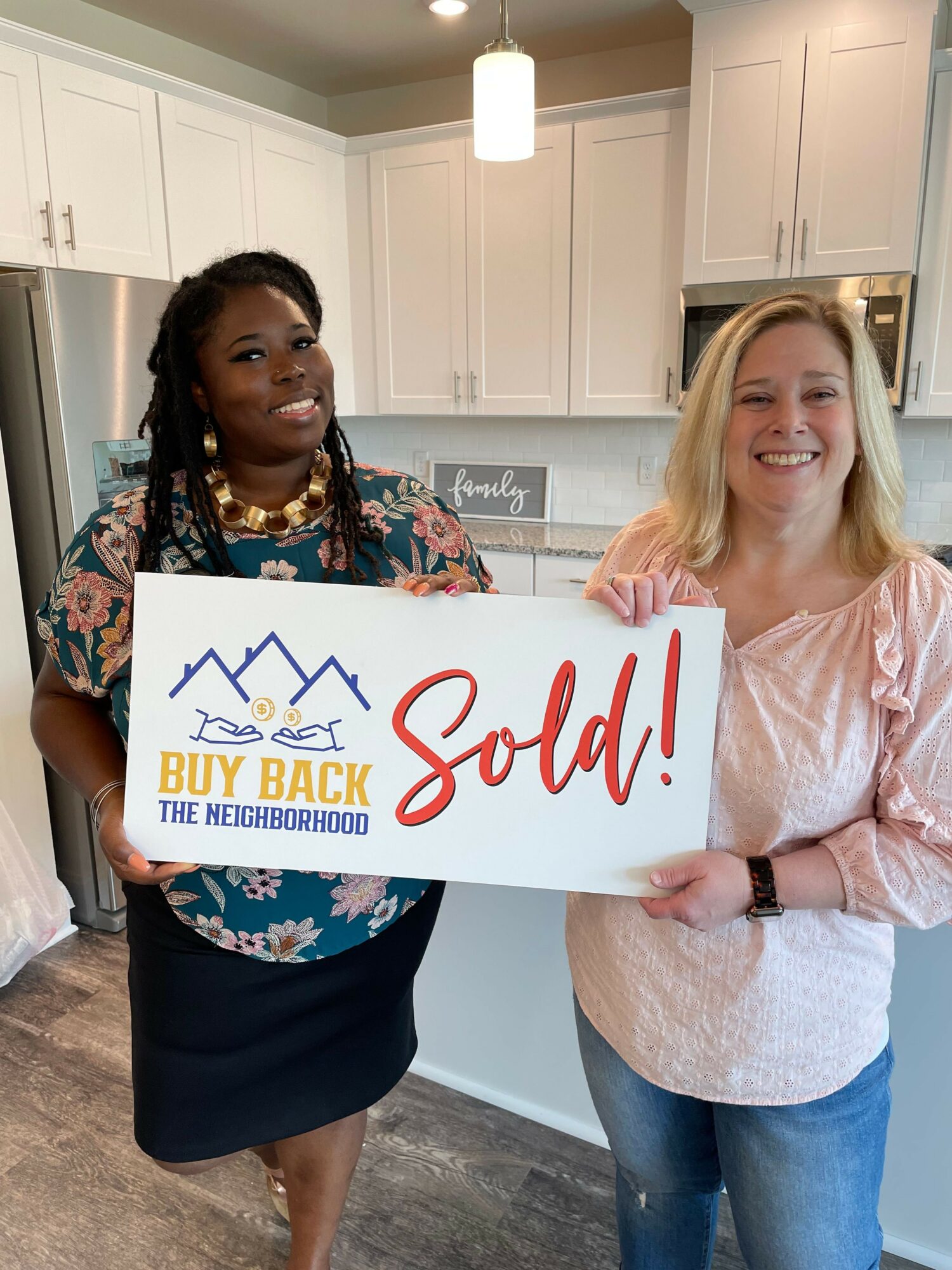 Two women standing indoors, one holding a sign that says 'God! Buy Back the Truck!'.