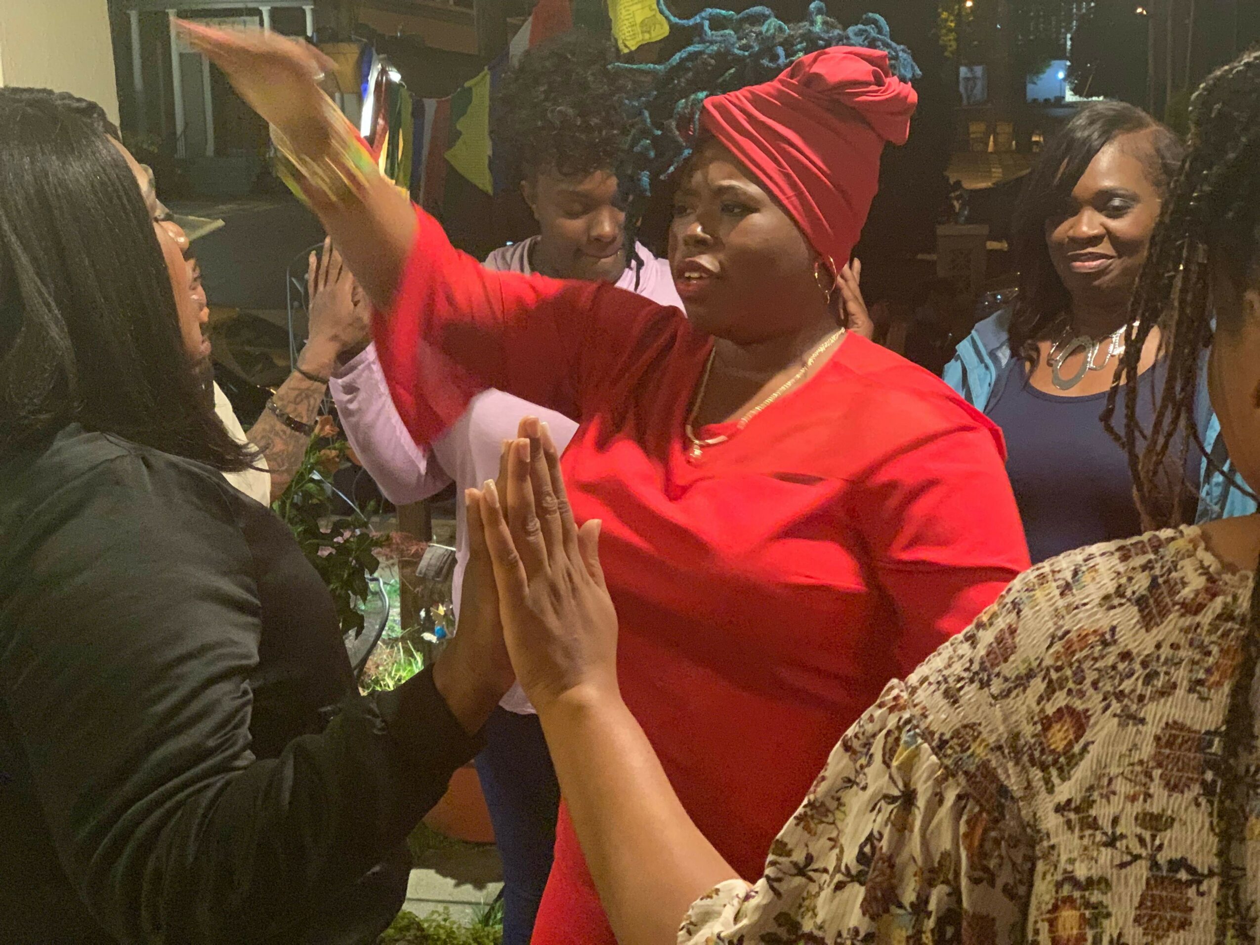People gathered around a table, with one person in a red outfit and headscarf, engaging in an activity.