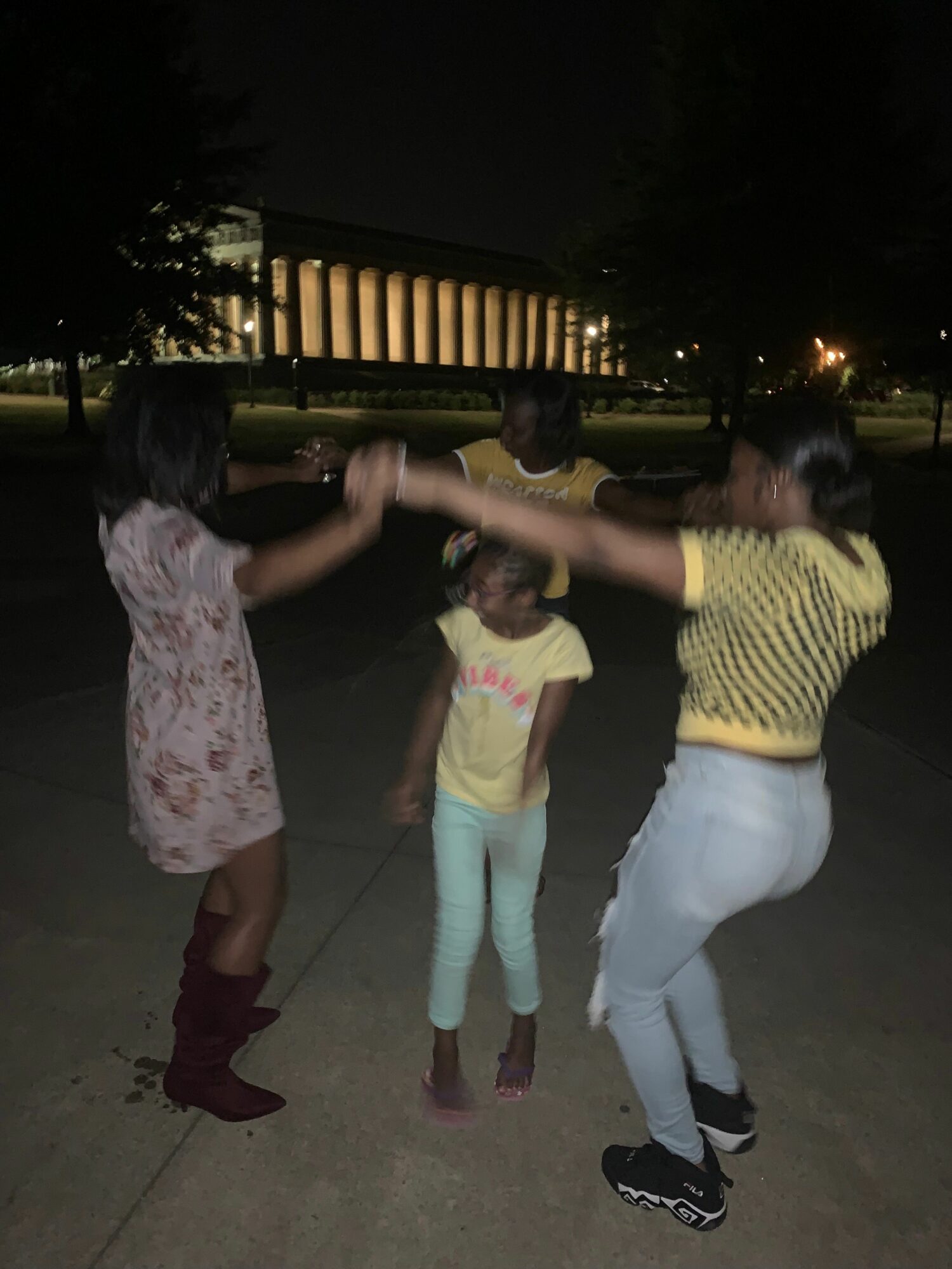 Three people, two children and an adult, holding hands and walking on a sidewalk at night.