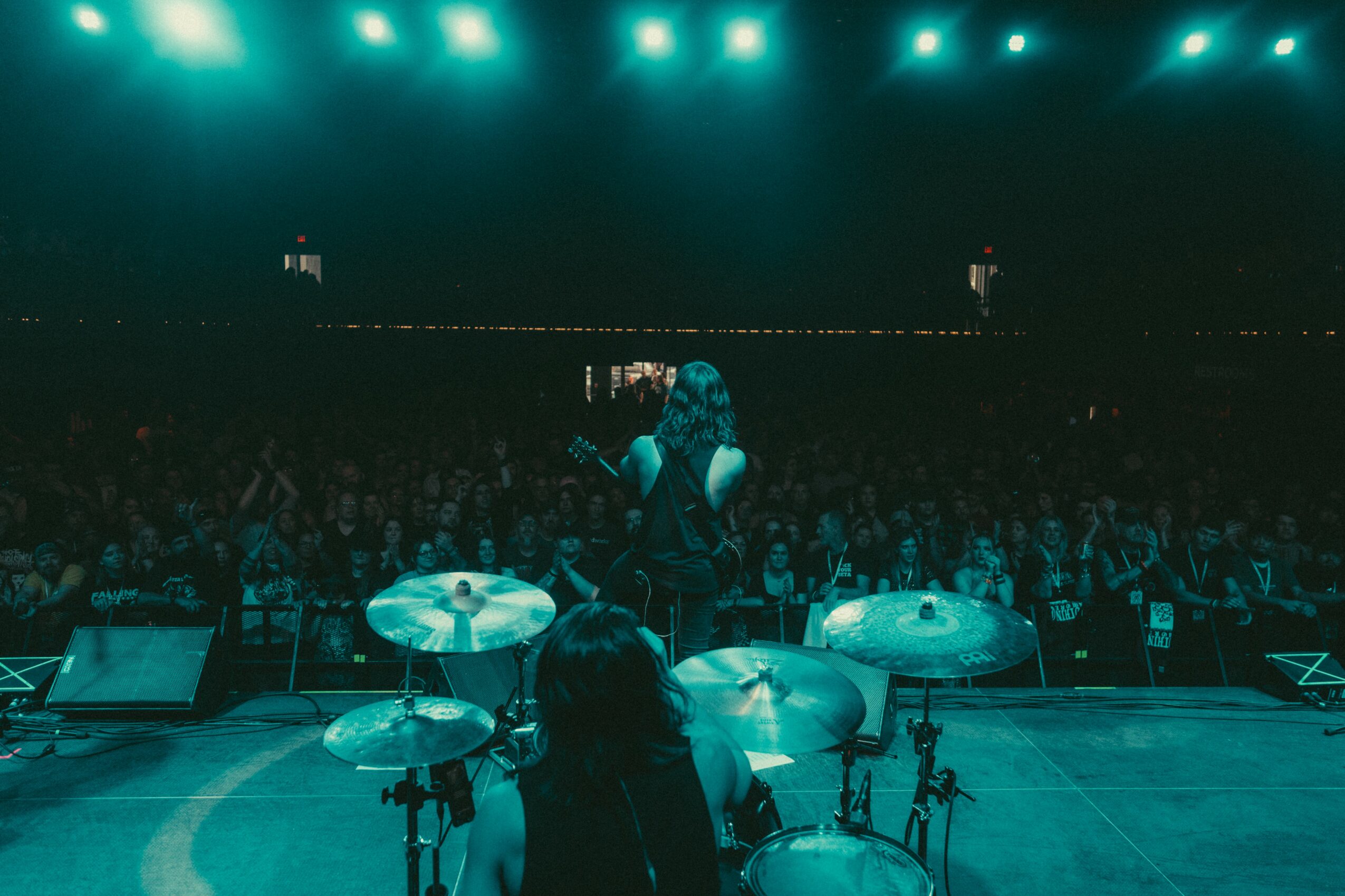 Performer singing on stage with drums and audience in background, illuminated by green stage lights.