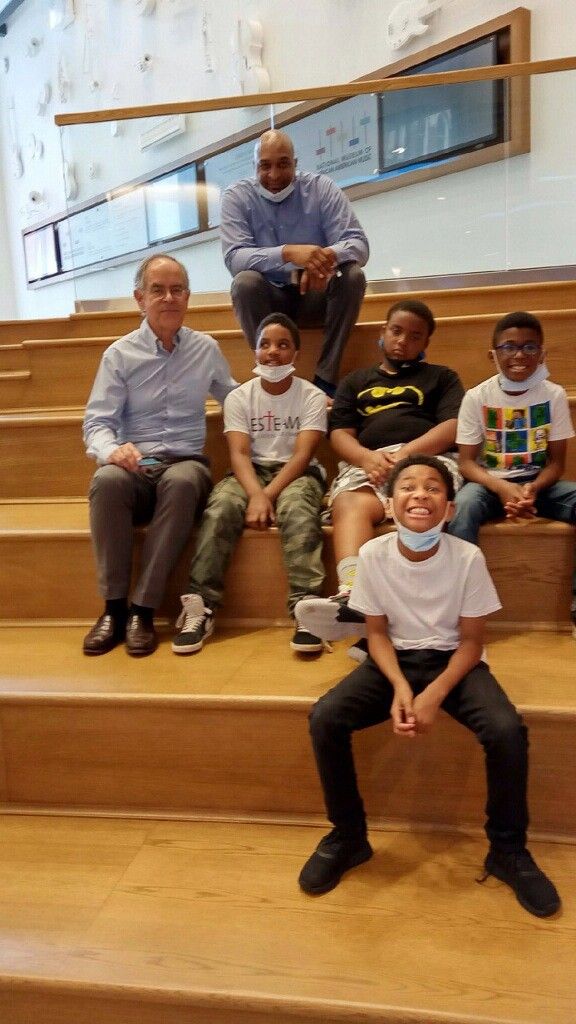Group of six people, five children and one adult, sitting on wooden stairs indoors, smiling at the camera.