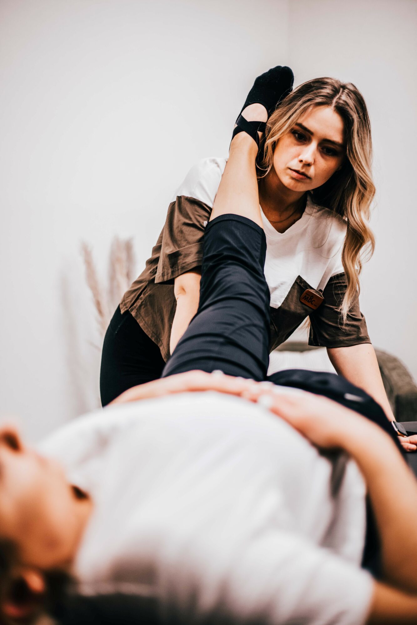 Woman with long hair looking at a person lying down, with a hand on her head, in a clinical setting.