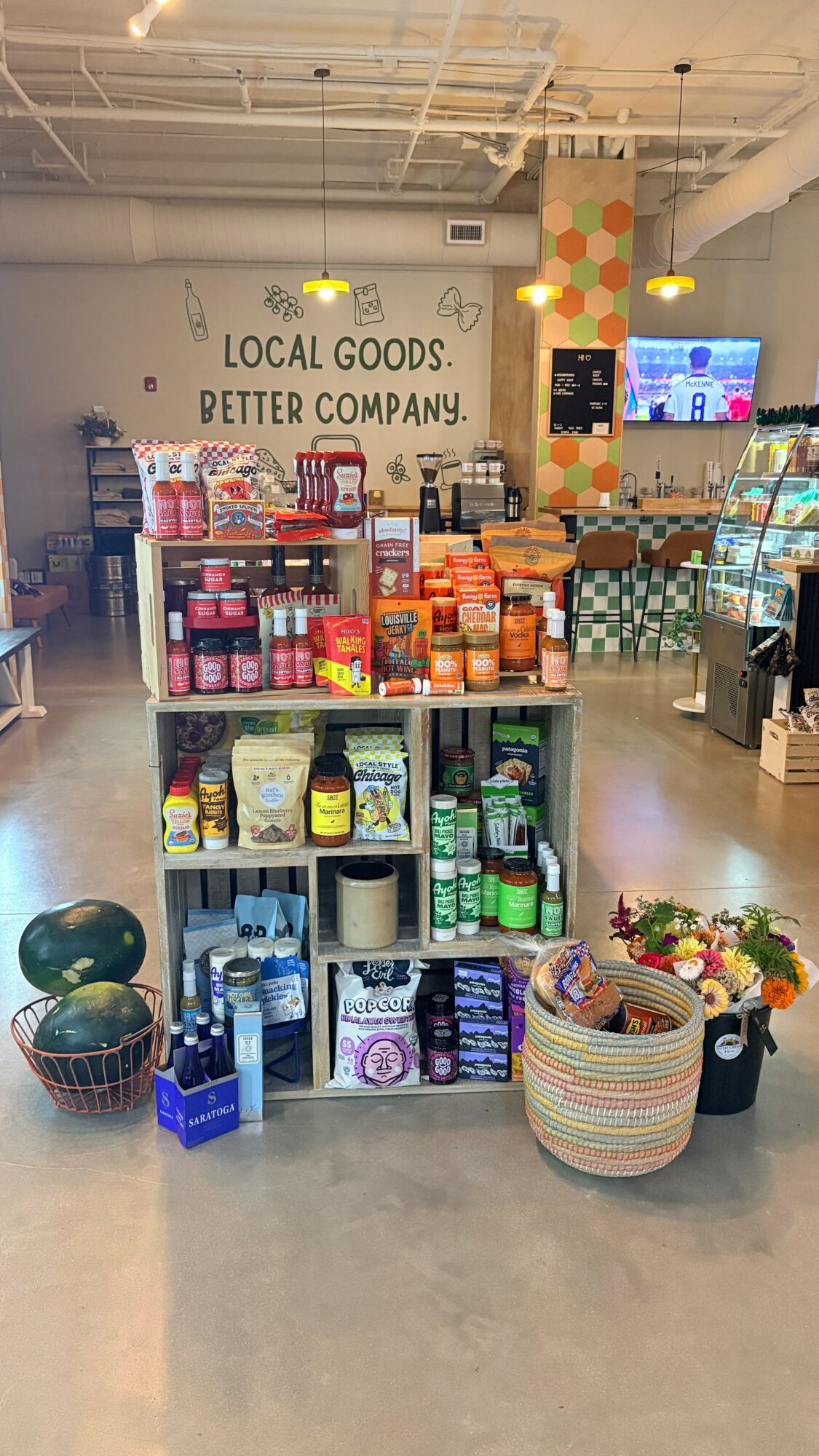 Display shelf with various products in a store, with a colorful wall and TV in the background.