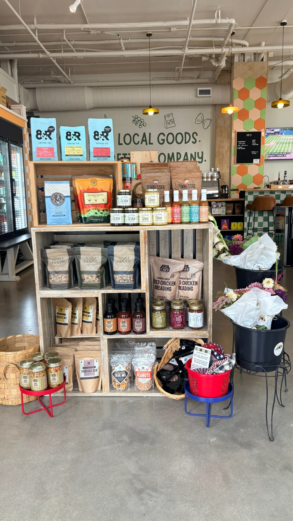 Shelves with local goods, jars, and boxes in a store, with colorful decorations and a sign in the background.