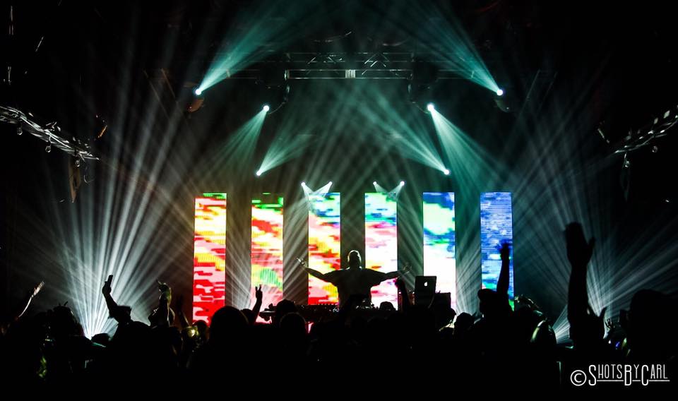 Concert scene with colorful vertical screens, stage lights, and audience raising hands, silhouette visible.