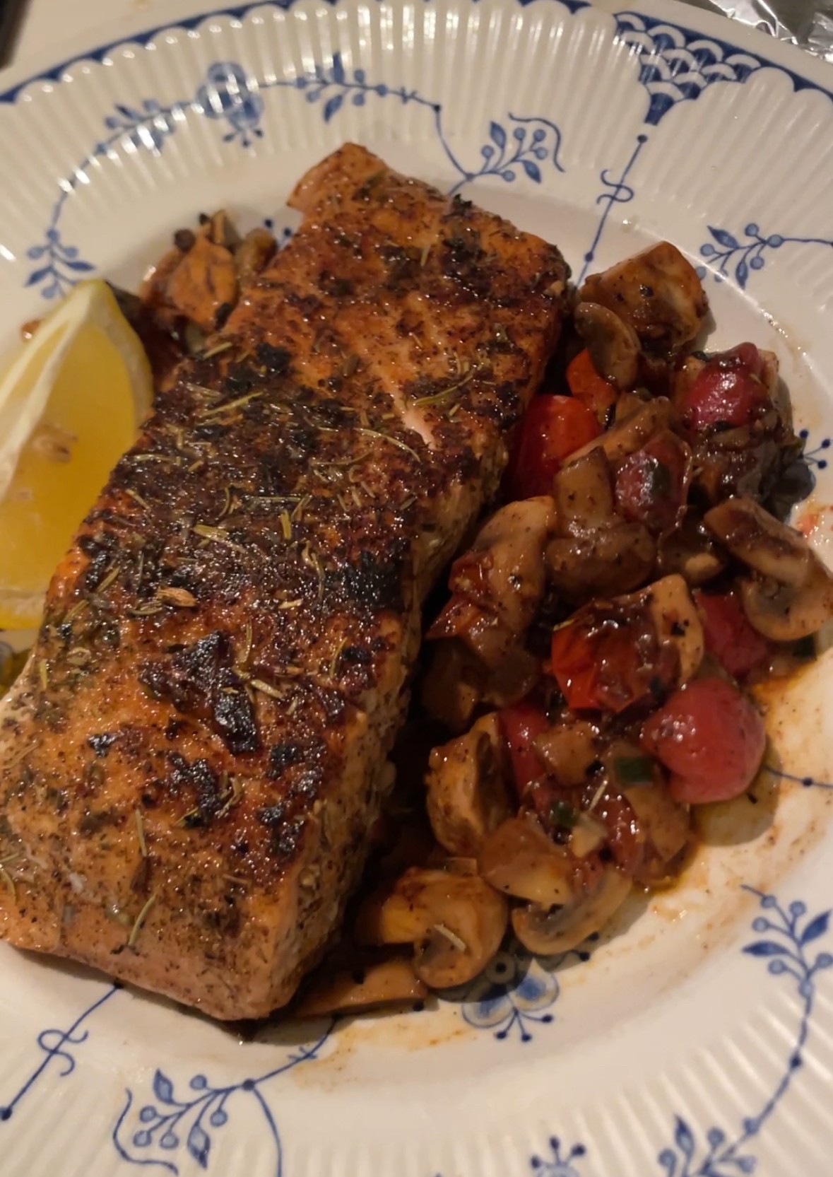 Grilled fish fillet with a side of sautéed vegetables and a lemon wedge on a decorative plate.