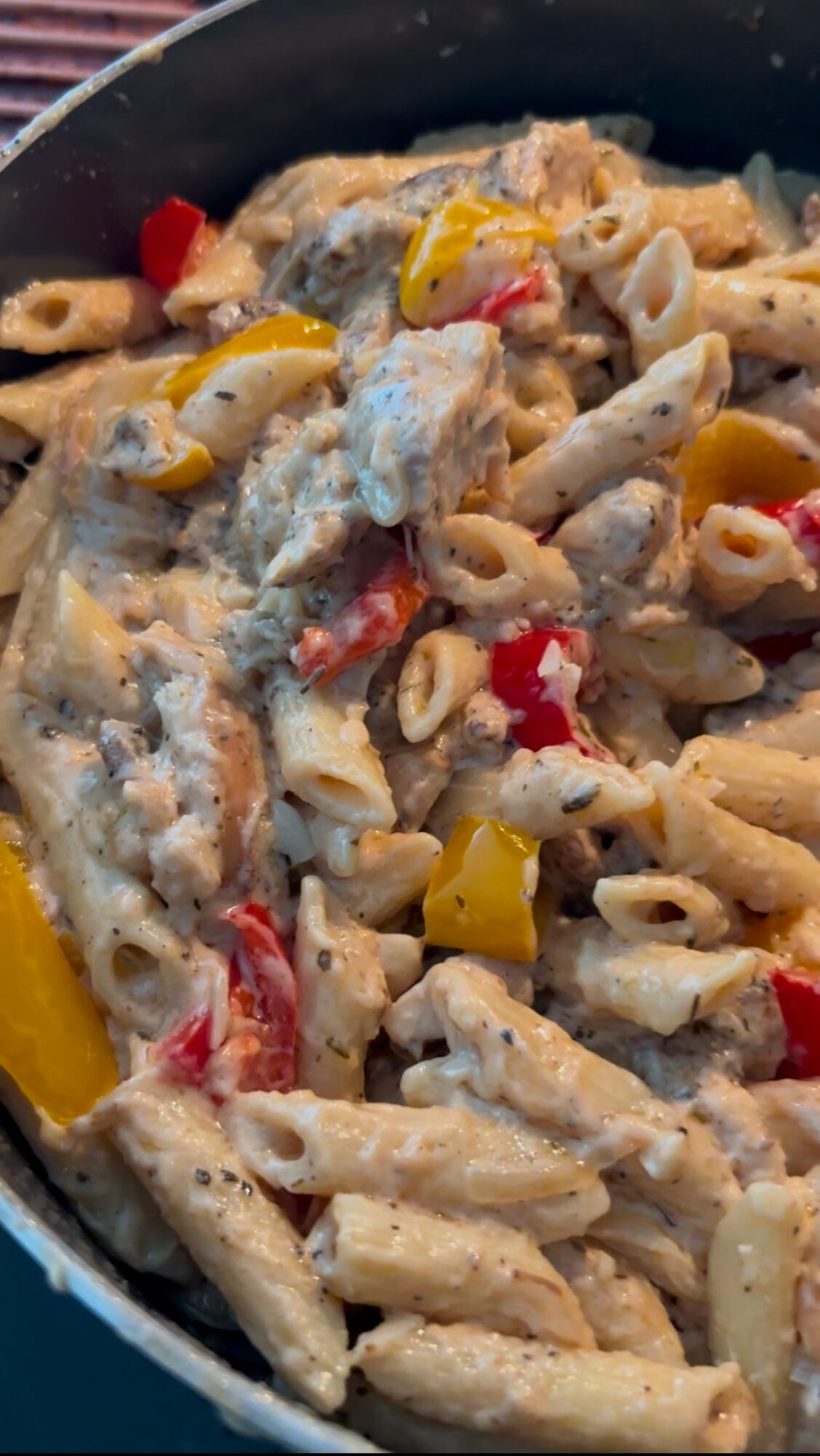 Pasta with vegetables and creamy sauce in a pan, including red and yellow peppers, and possibly chicken or fish.