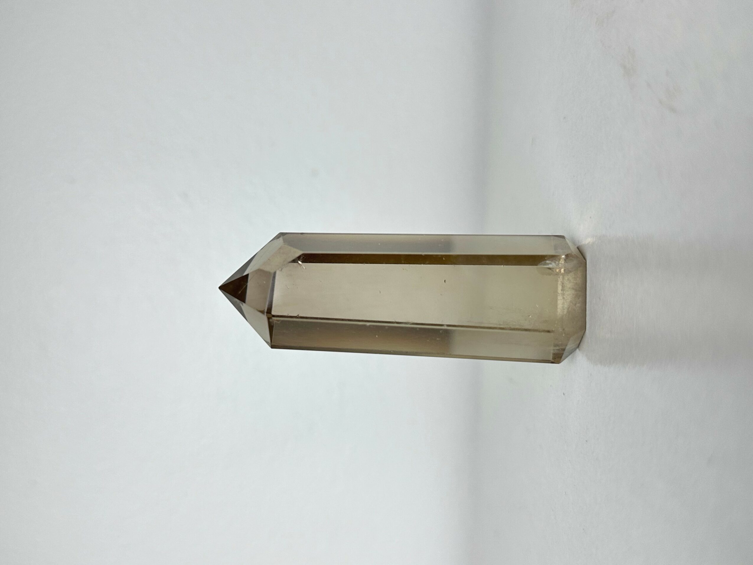 A clear, hexagonal prism-shaped object with a pointed tip, placed on a white surface with a plain background.