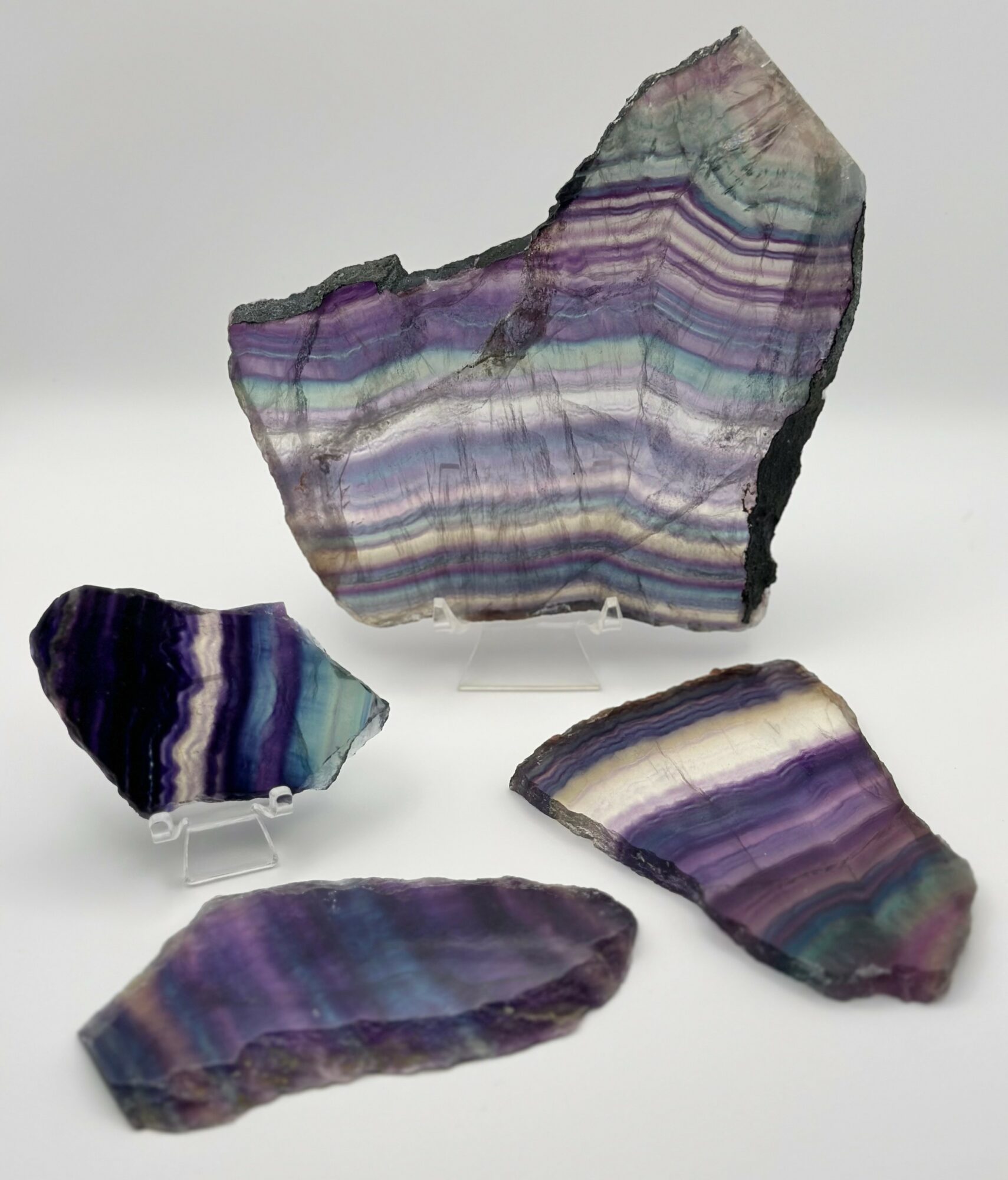 Four colorful, layered mineral or gemstone fragments with purple, green, and white bands on a white background.
