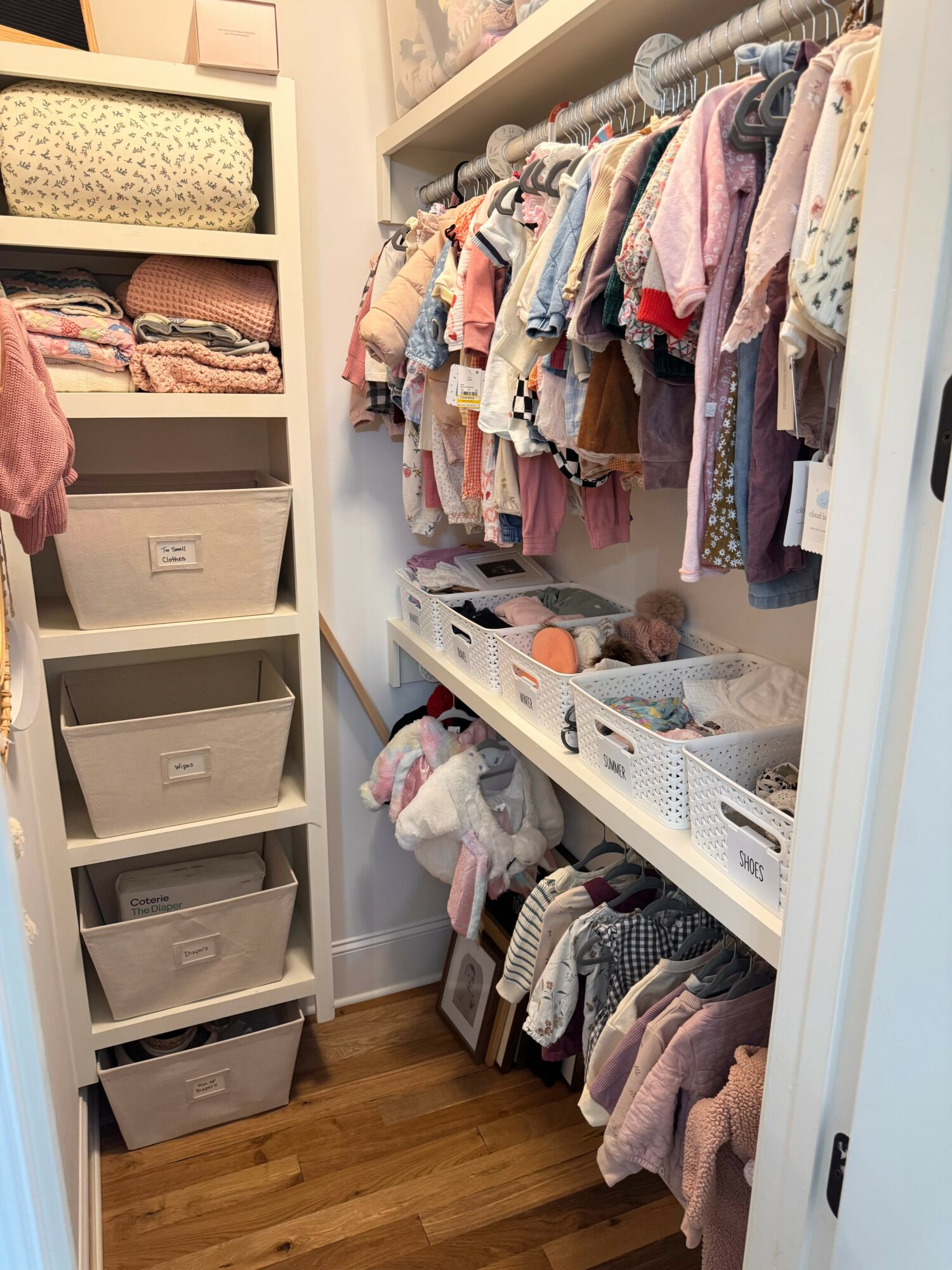 Closet with hanging clothes, shelves with folded items, and plastic bins for storage, all organized neatly.