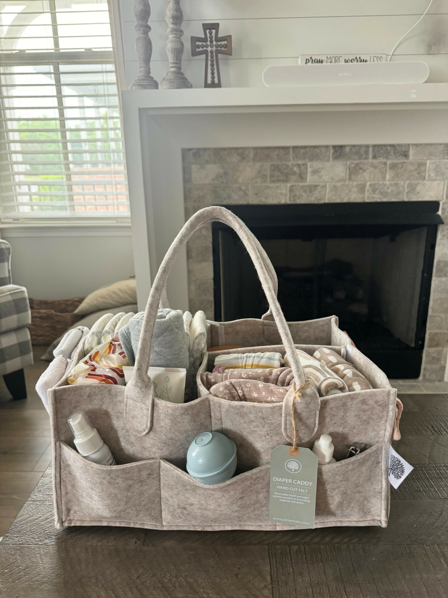 Organized fabric caddy with rolled towels and toiletries in front of a fireplace, window with blinds in background.
