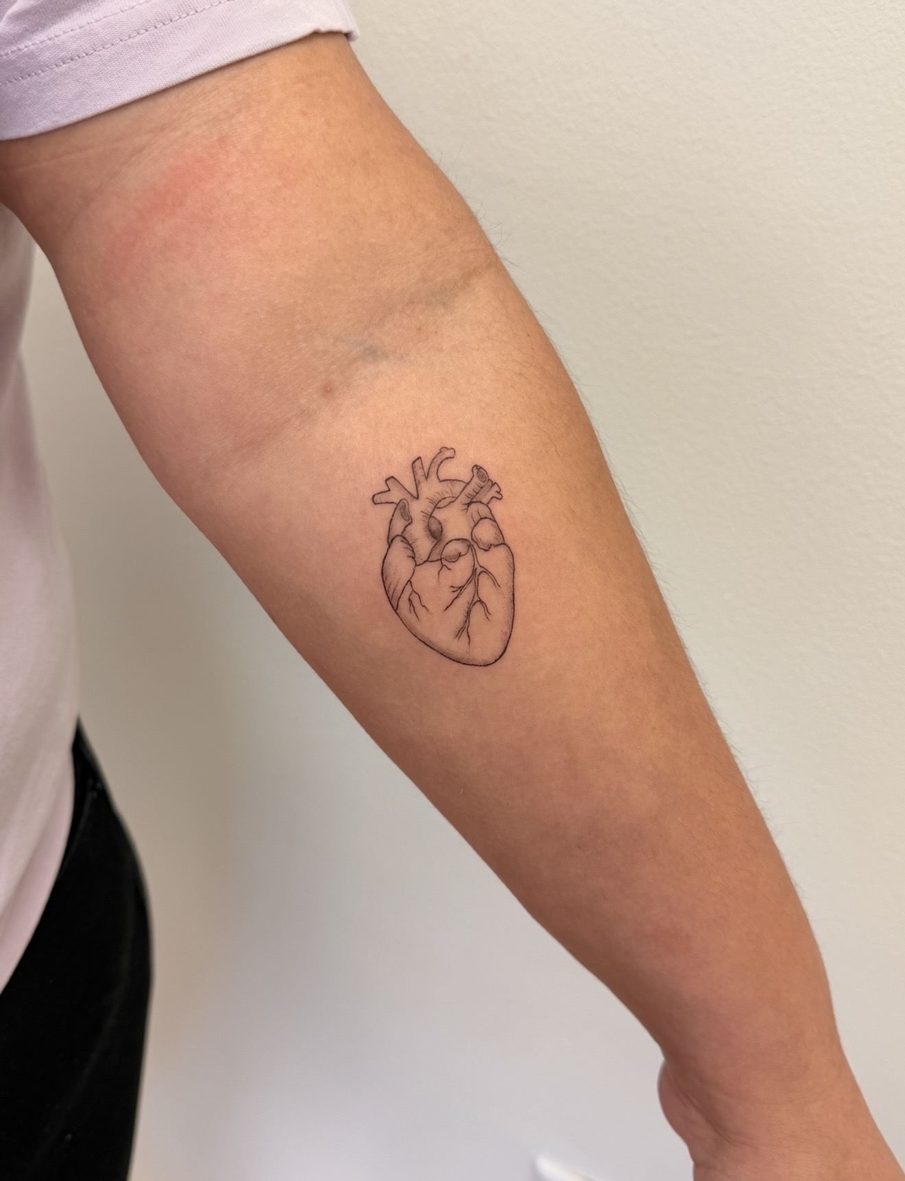 Tattoo of a human heart on person's upper arm, with visible veins and skin texture, against a plain background.
