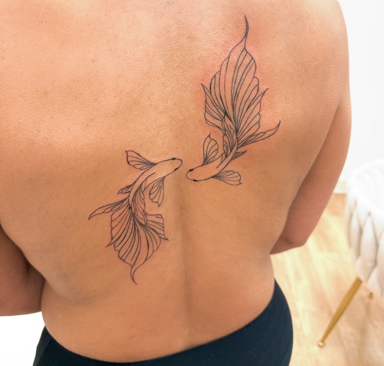 Two fish swimming towards each other with flowing fins and tails, tattooed on a person's back, upper right side.