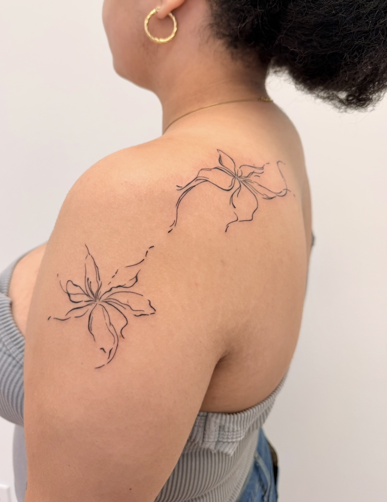Person with two butterfly tattoos on shoulder, wearing a gold hoop earring and striped top, facing left.