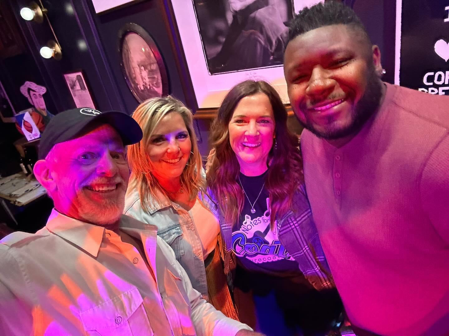 Four people smiling for a photo indoors, with colorful background and framed pictures, in a lively setting.