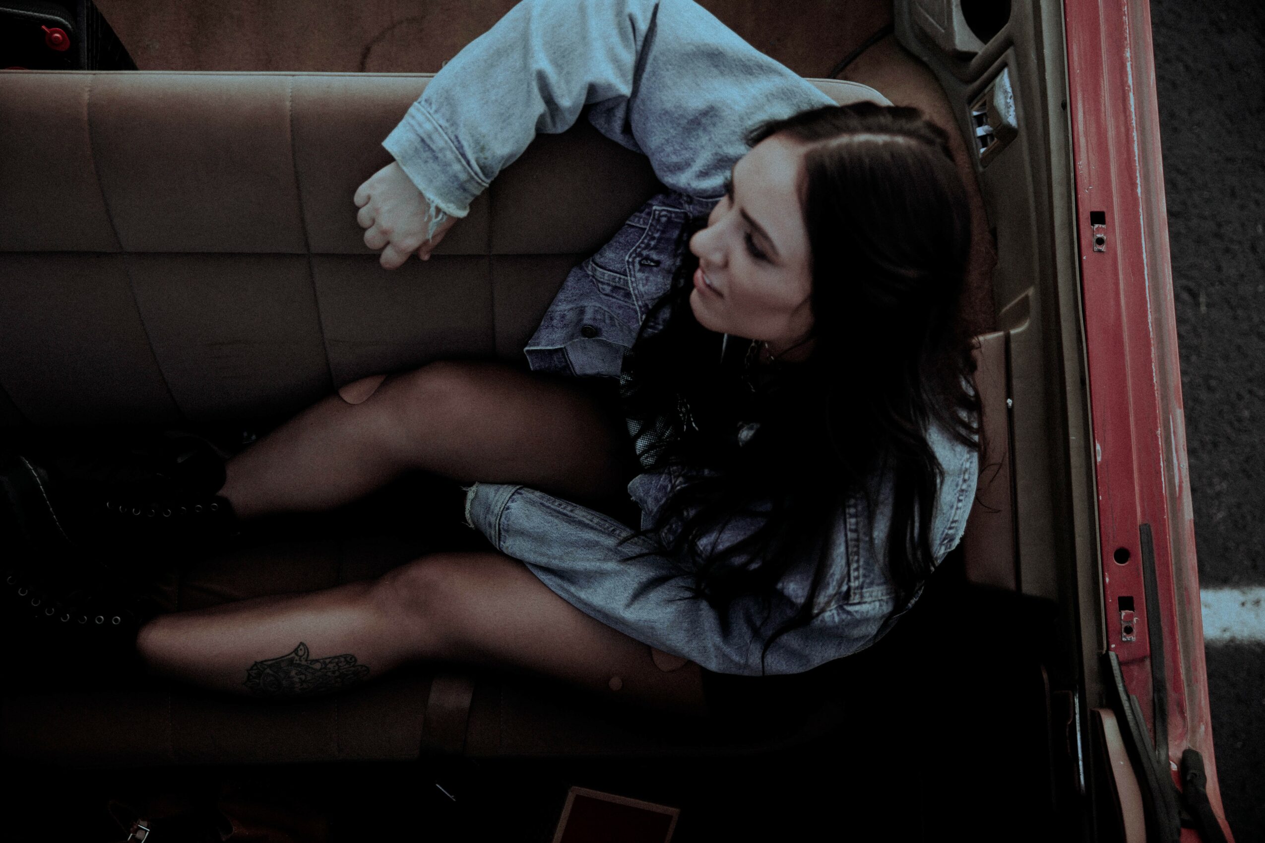 A woman with long dark hair sitting in a car, looking to the side, with a child lying on her lap.